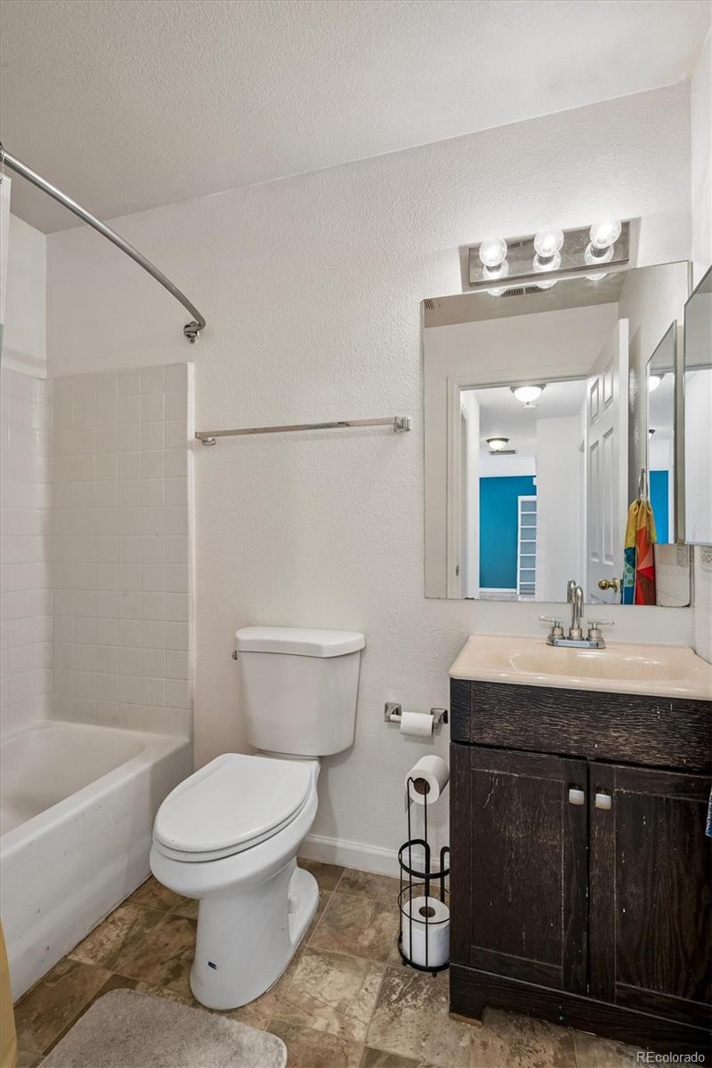 Bathroom with a white tub and shower, toilet, dark wood vanity, and mirror reflecting a blue wall.
