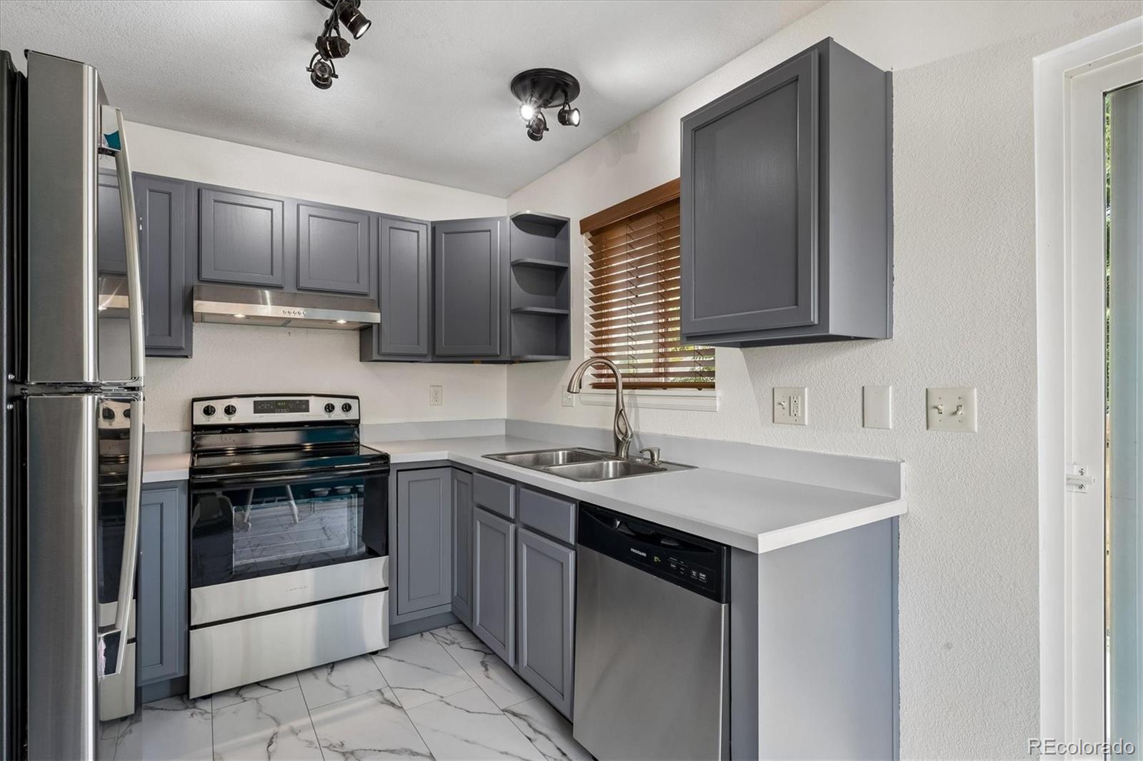 Kitchen with gray cabinets, stainless steel appliances, white counters, and marble-look tile flooring.