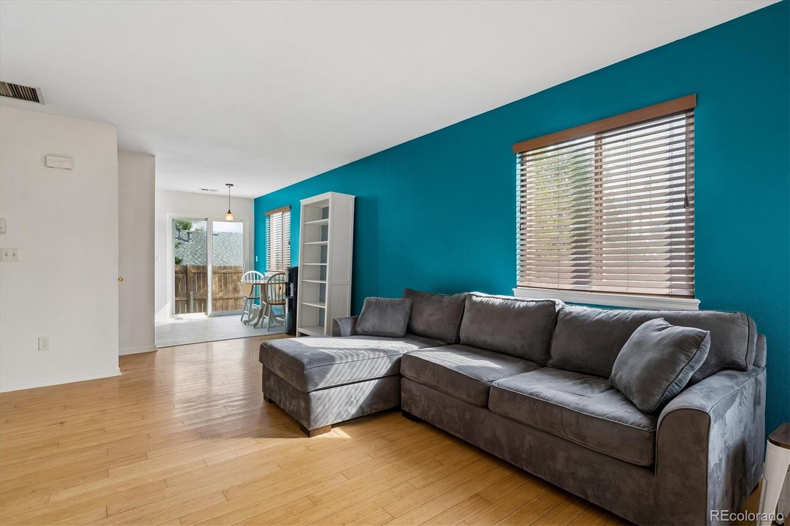 Living room with a gray sectional, turquoise accent wall, wood floors, and sliding glass doors.