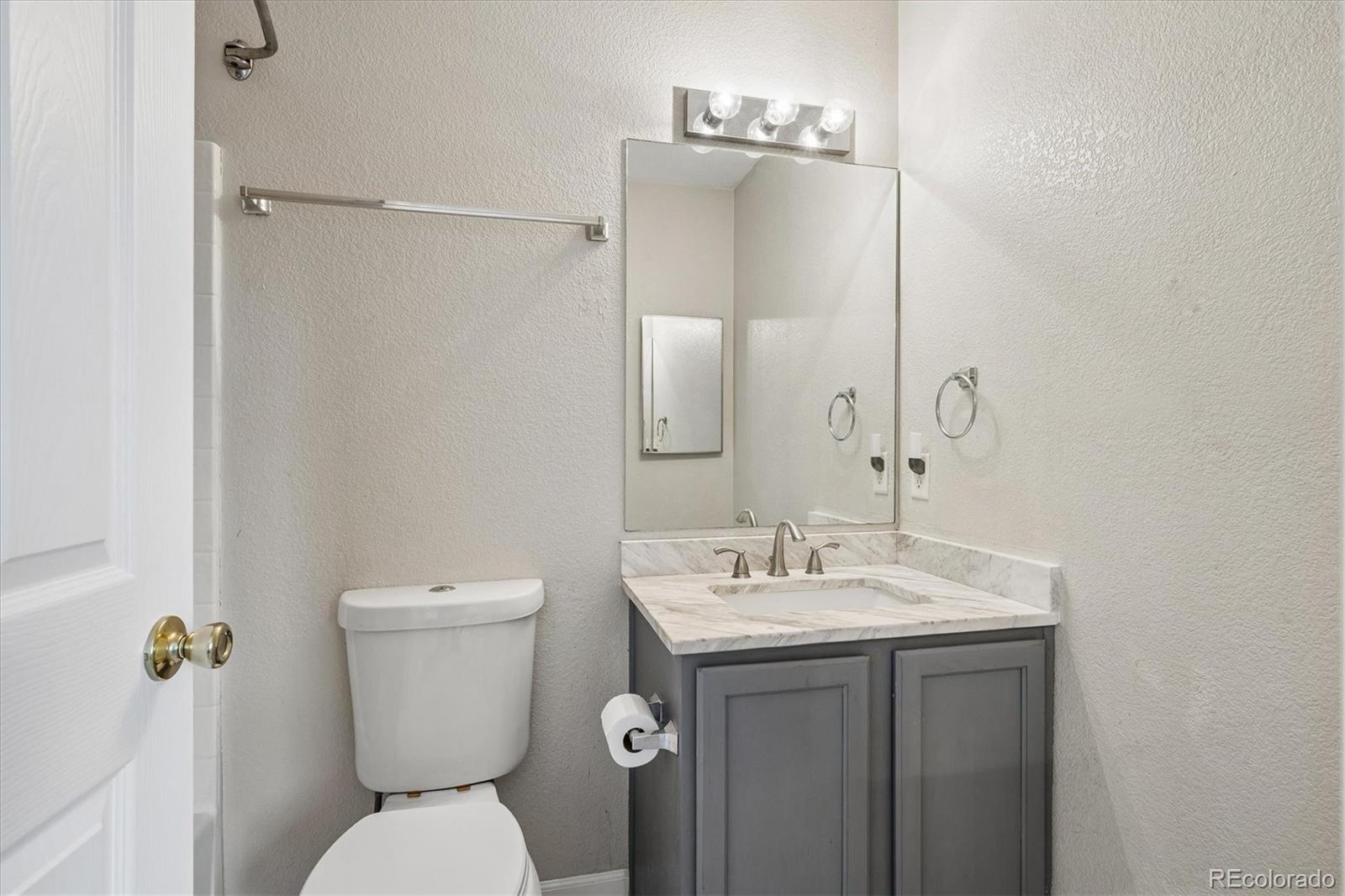Bathroom with a gray vanity, marble-look counter, large mirror, and toilet.