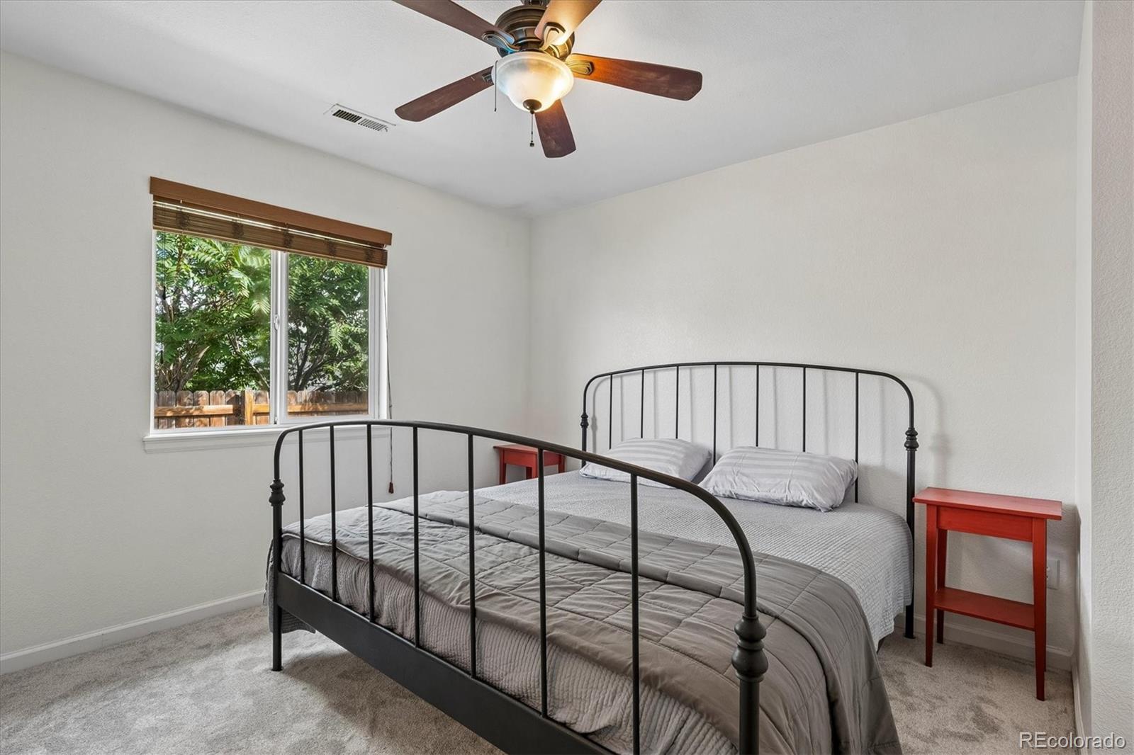 Bedroom with a black metal bed, gray bedding, and a window overlooking leafy trees.