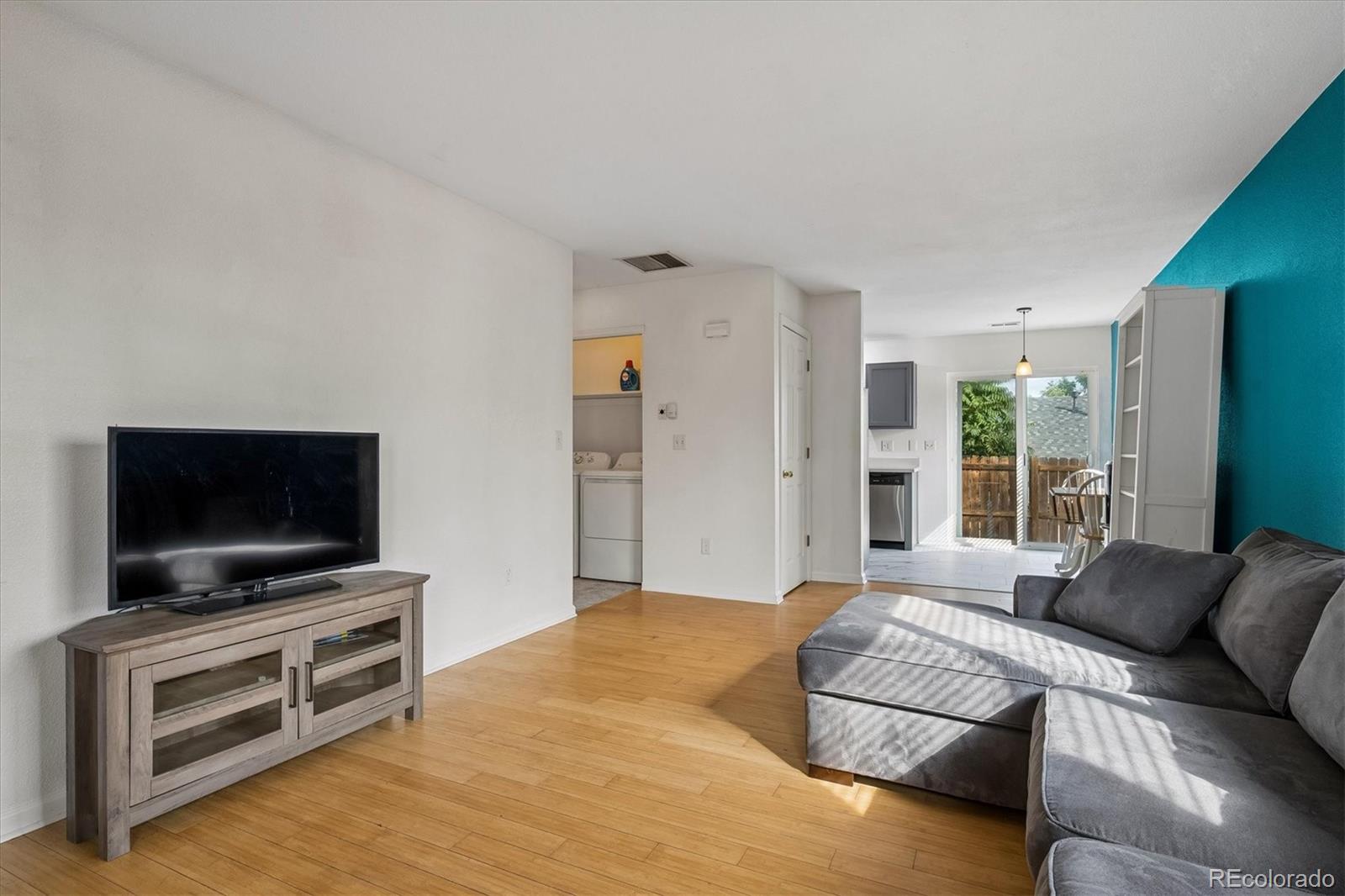 Furnished living room with a gray sectional, wood floors, and a teal accent wall.