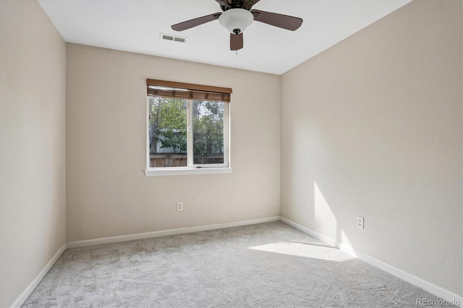 Empty bedroom with gray carpet, a ceiling fan, and a window with wooden blinds.
