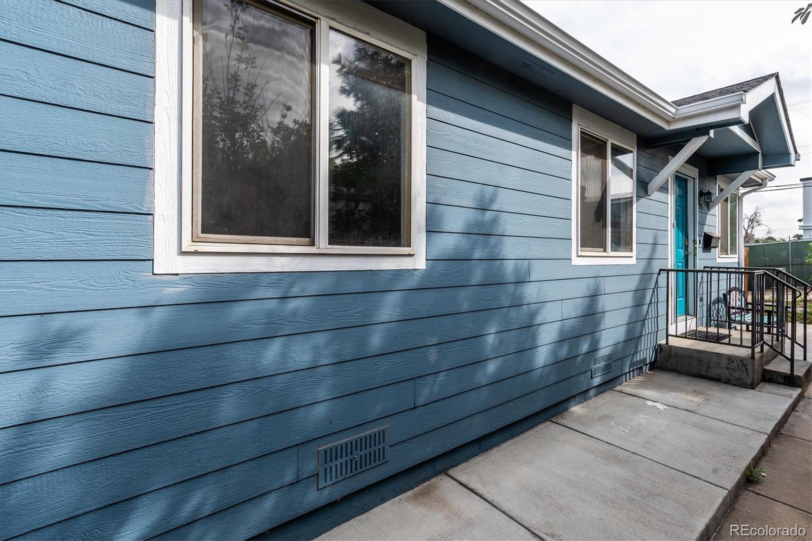 Blue house exterior with white-trimmed windows, turquoise entry door, and black metal railings.