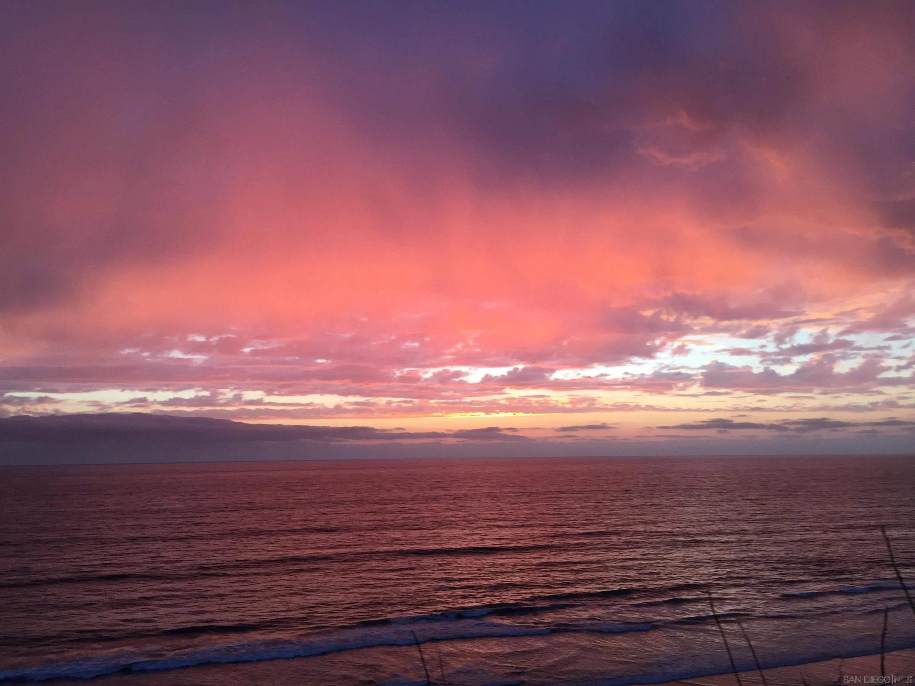 Vibrant ocean sunset from backyard of 194 Neptune Avenue-Encinitas-CA-92024 featuring pink, orange, and purple skies reflecting over calm waves in this serene coastal setting listed by FW Property Group