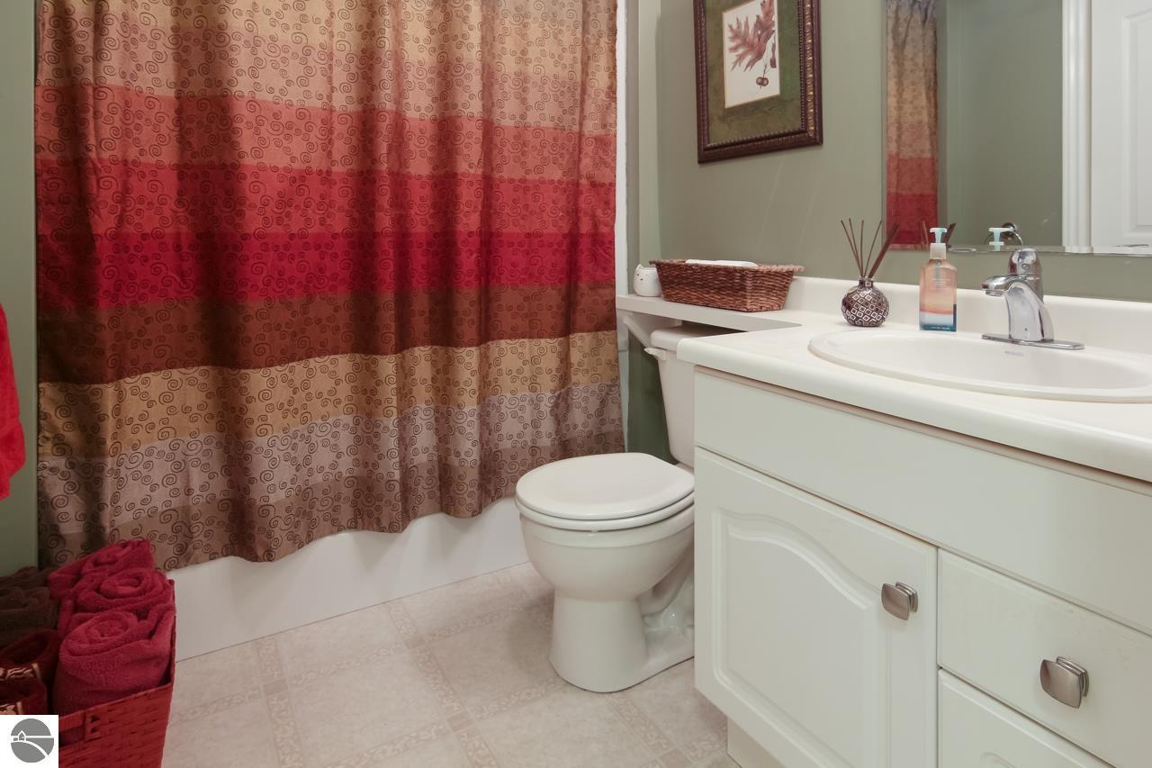 Bathroom with a white vanity and toilet beside a red-and-brown patterned shower curtain.