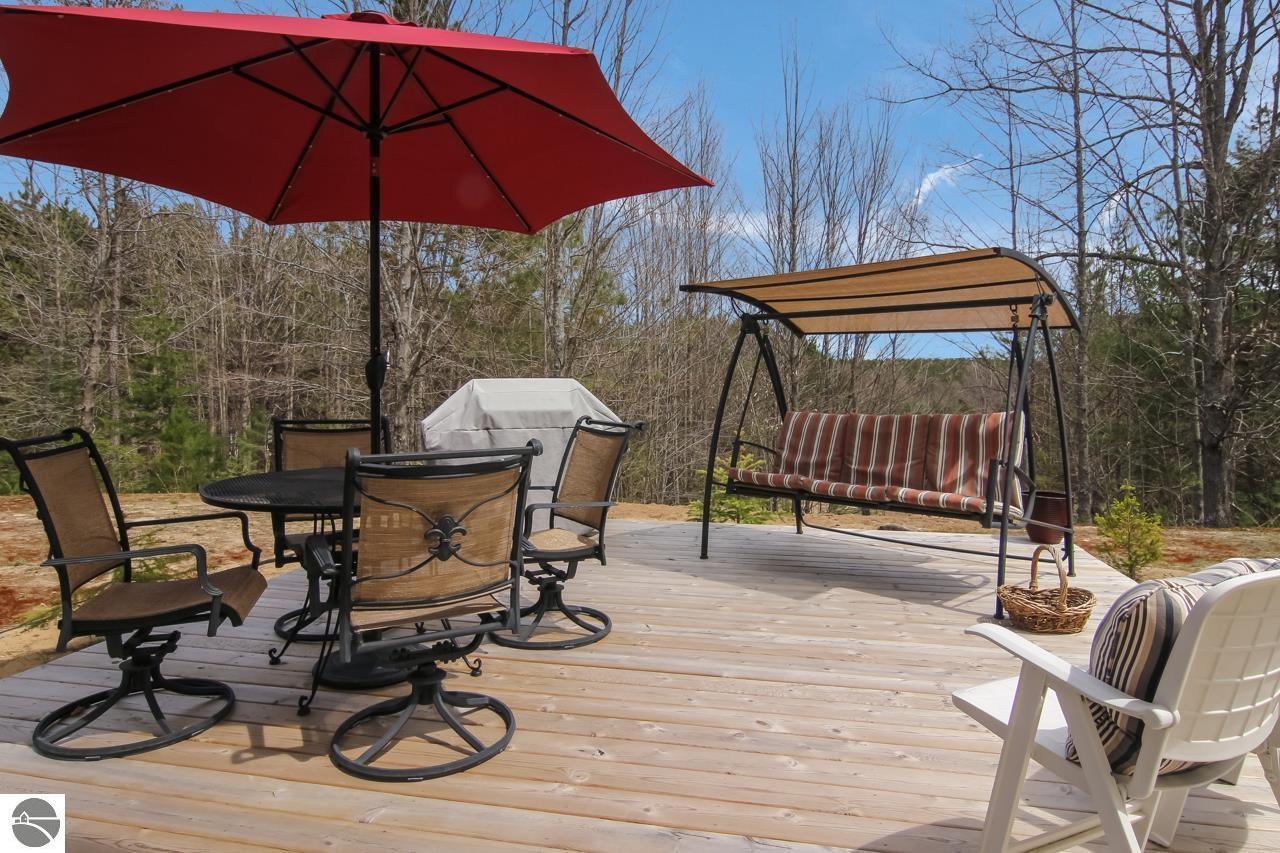 Wooden deck with a red umbrella, dining set, and covered swing overlooking leafless woods.
