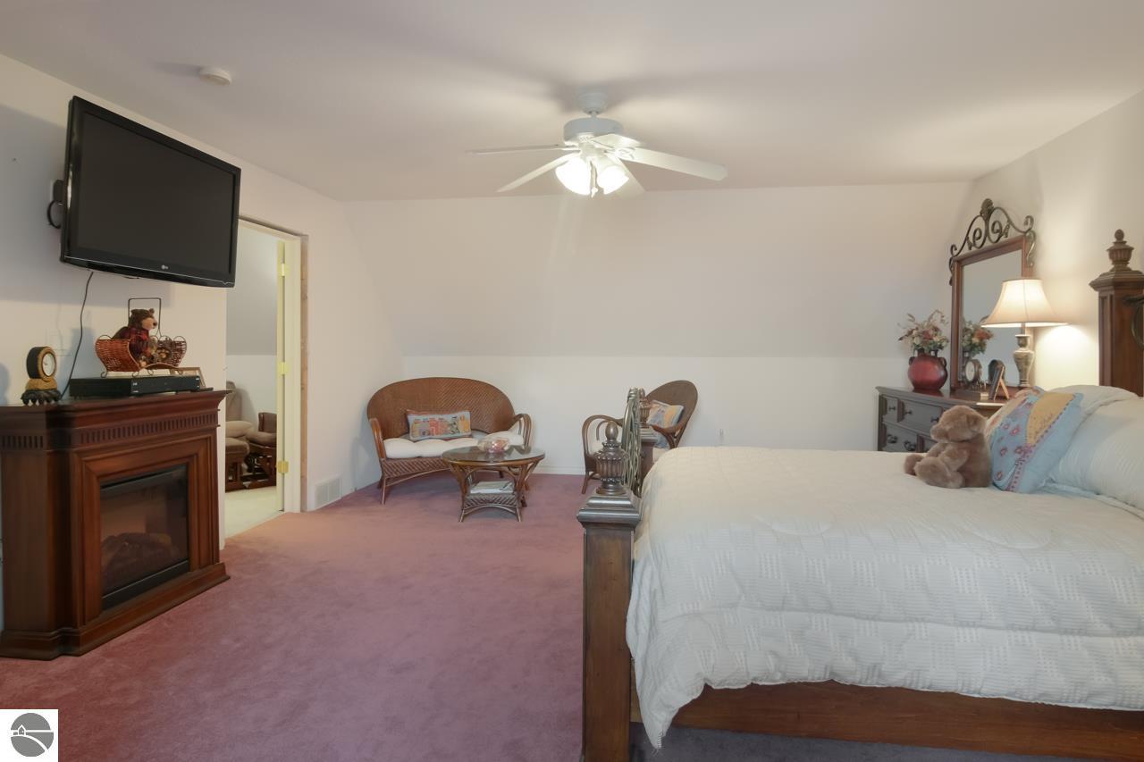 Furnished bedroom with a large bed, wicker seating, and a fireplace beneath a wall-mounted television.
