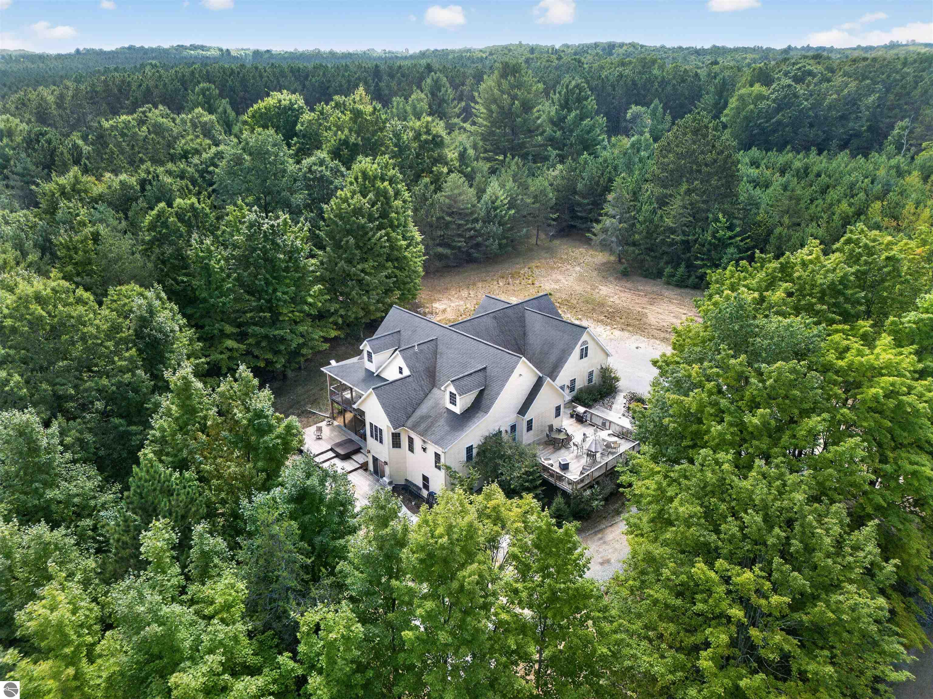 Aerial view of a multi-gabled home and decks surrounded by dense woodland.
