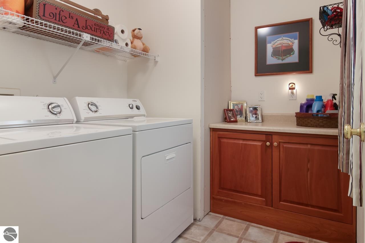 Laundry room with white washer and dryer beside reddish wood cabinets and a countertop.