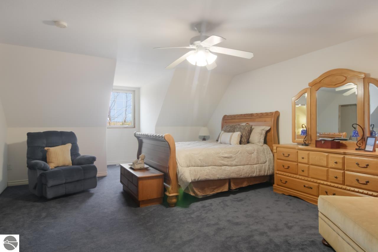 Furnished bedroom with a wooden bed, dresser, gray recliner, and sloped ceiling.