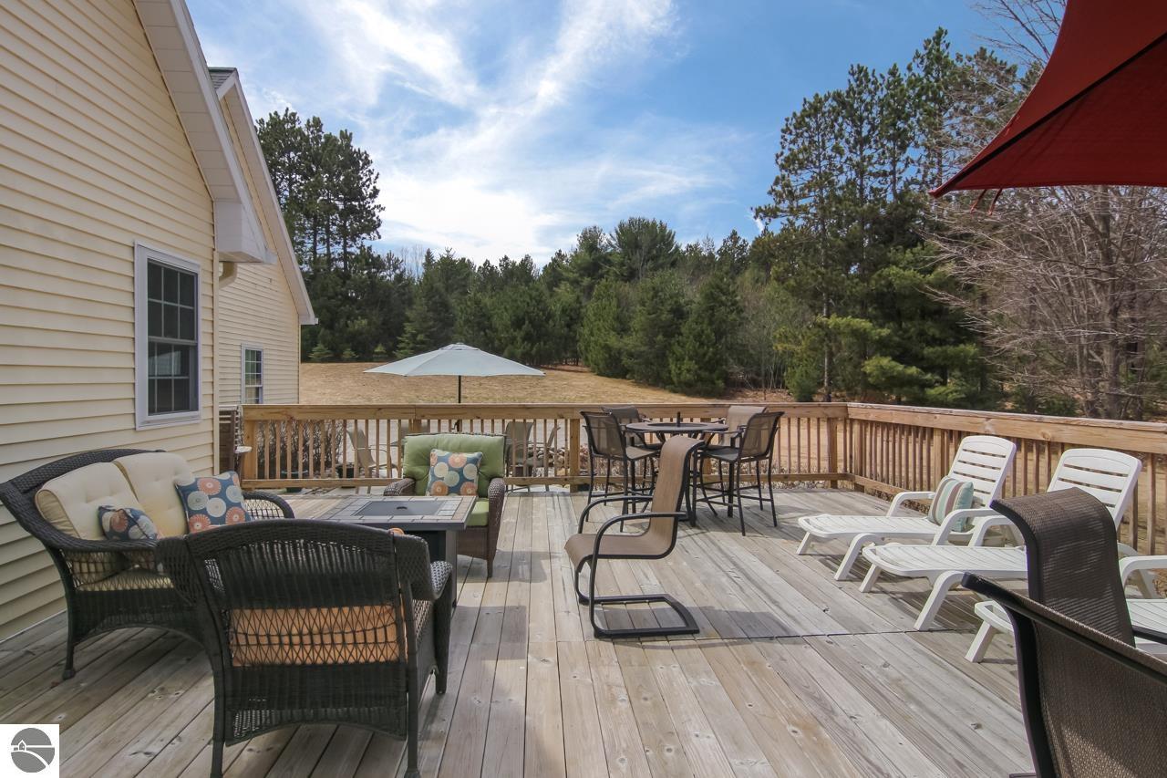 Furnished wooden deck with lounge chairs and dining table overlooking a lawn and trees.