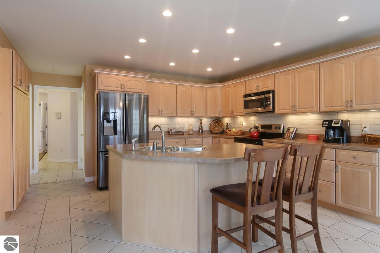 Spacious kitchen with a large sink island, light wood cabinets, stainless steel appliances, and bar stools.