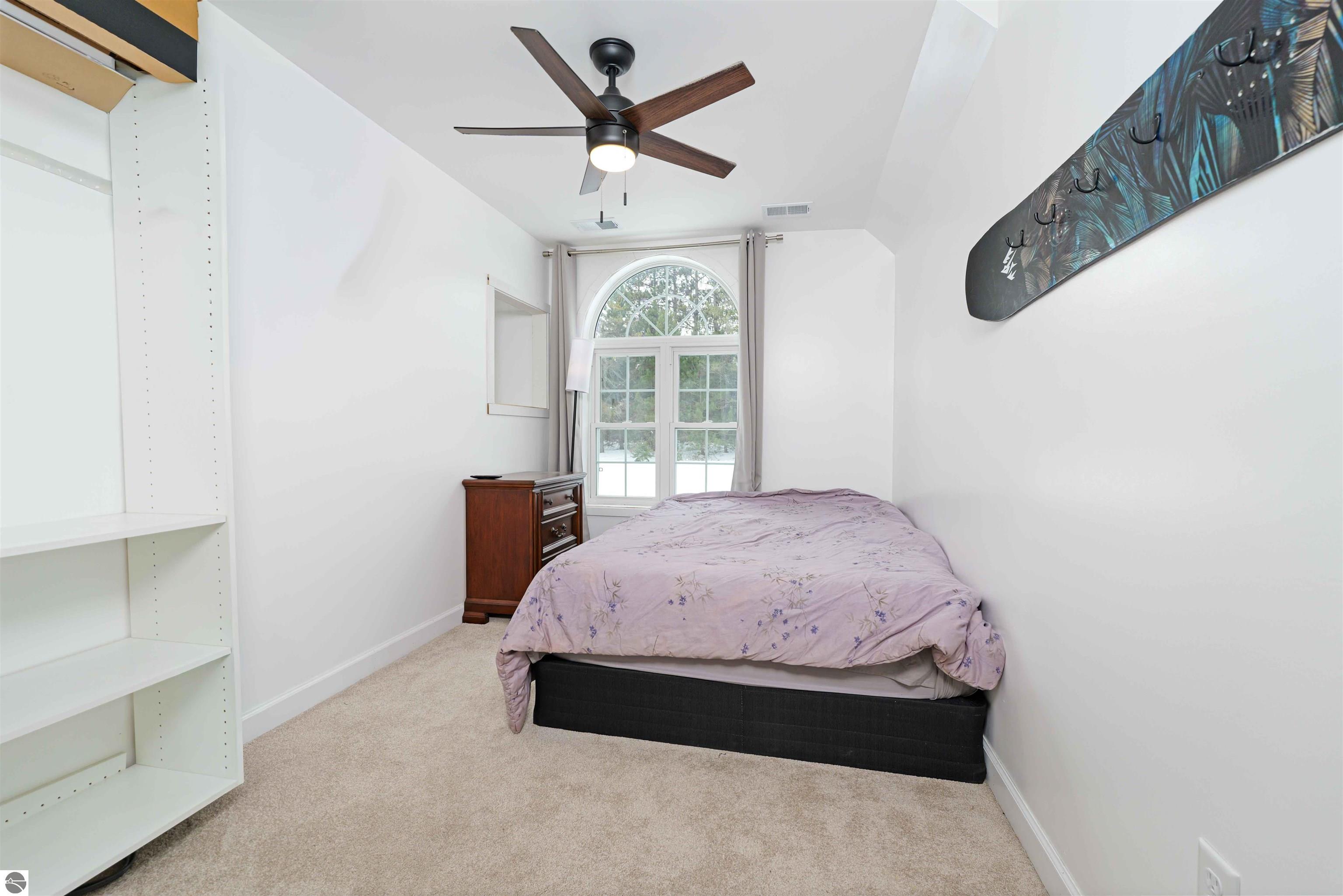 Furnished bedroom with a bed beneath a tall arched window and built-in white shelving.