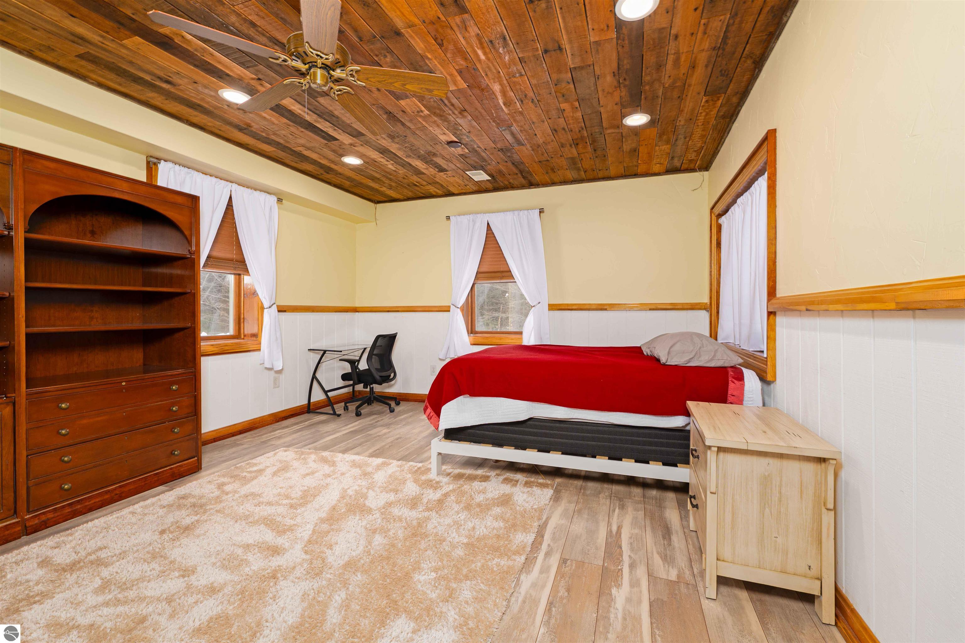 Bedroom with a red bedspread, wood-plank ceiling, and built-in shelving.
