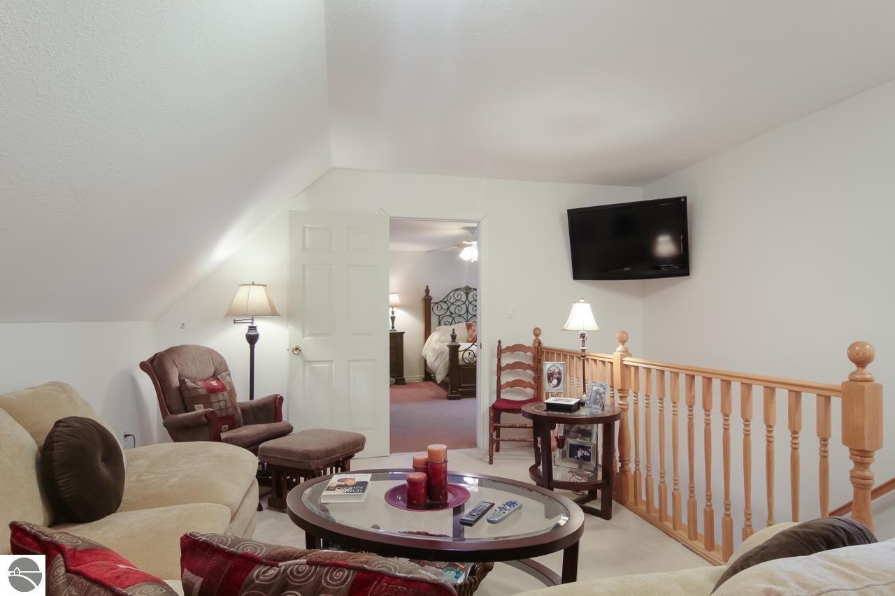 Upstairs sitting area with beige sofas, a wall-mounted television, and a wooden stair railing.