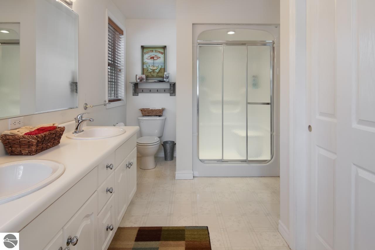 Bathroom with a double-sink vanity, frosted-glass shower, and striped window blind.