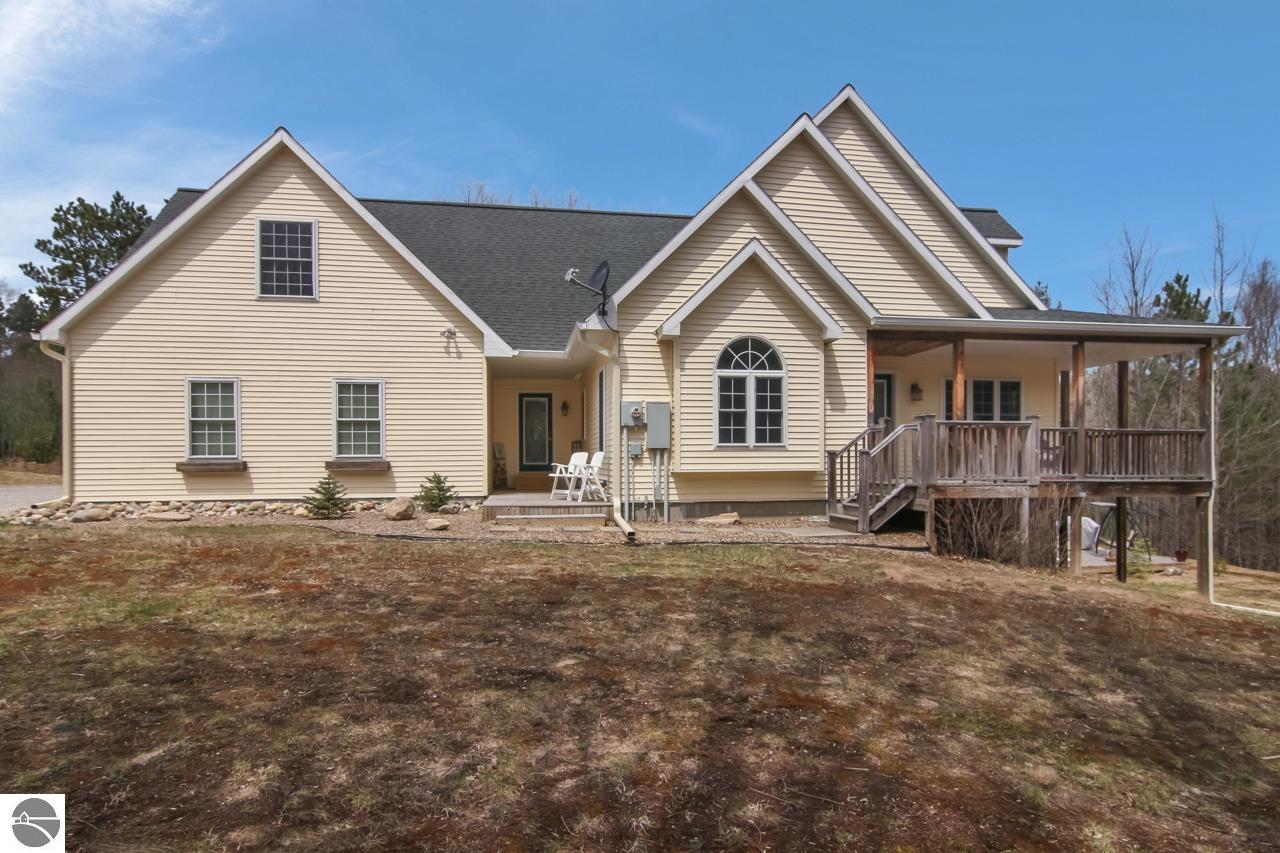Beige multi-gabled house with an arched window and raised covered wooden deck.
