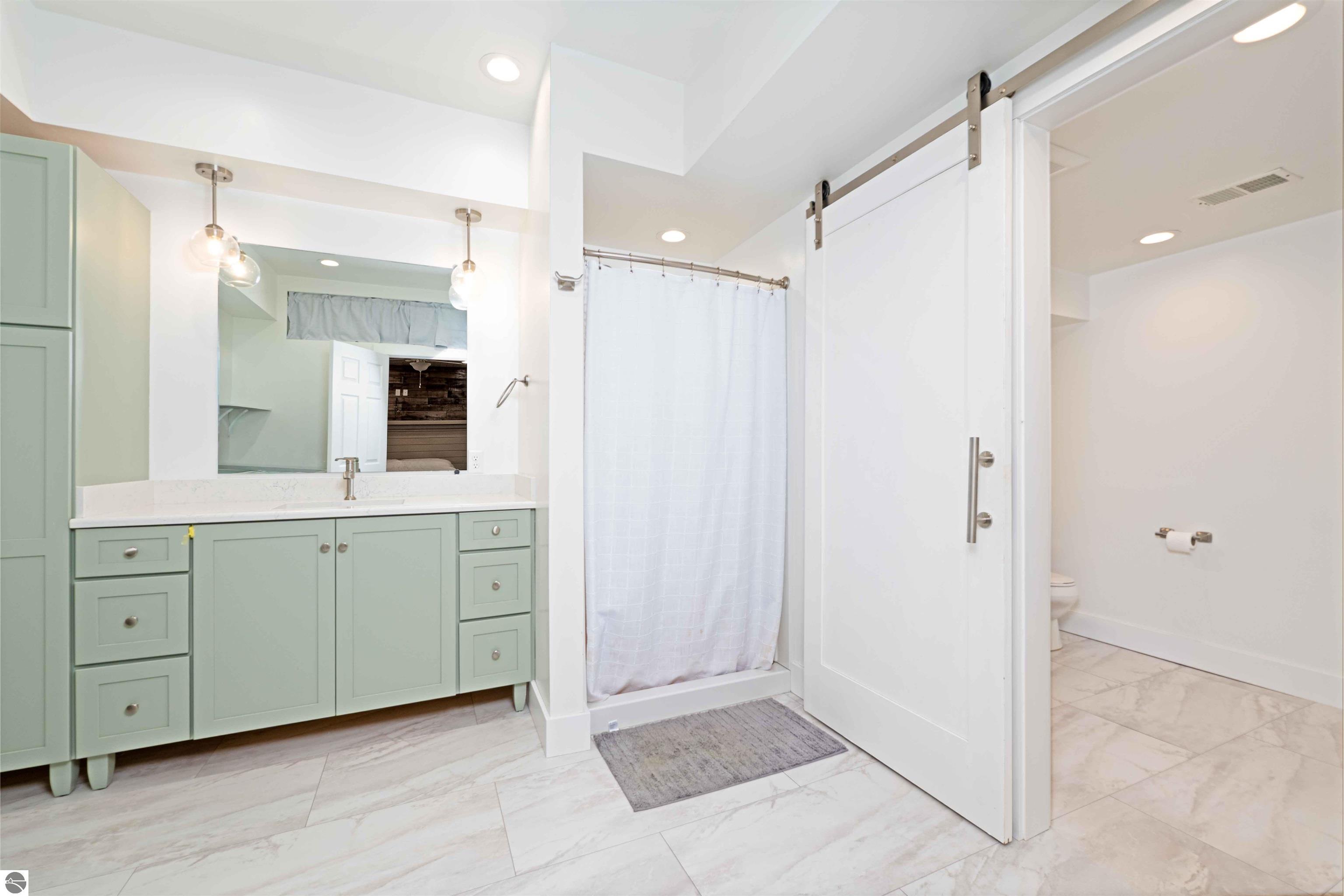 Bathroom with a sage-green vanity, curtained shower, and white sliding barn door.