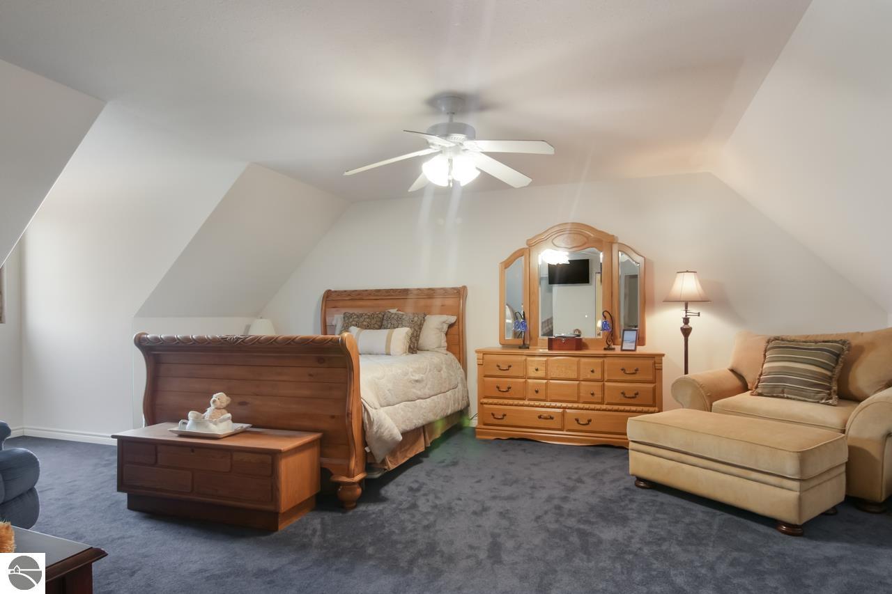 Attic bedroom with a wooden bed, matching dresser, beige sofa, and sloped ceiling.
