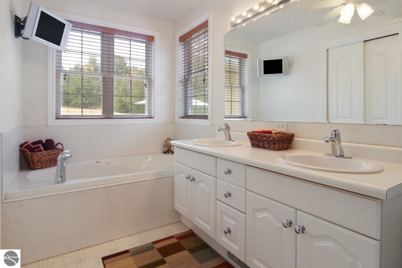 Bathroom with a built-in tub, double vanity, large mirror, and windows with blinds.