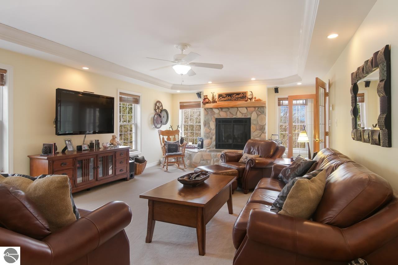 Furnished living room with leather seating, a rounded-stone fireplace, and a wall-mounted television.