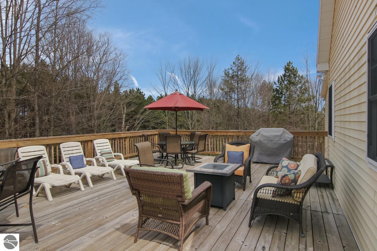 Furnished wooden deck with lounge seating, a red patio umbrella, and a wooded view.