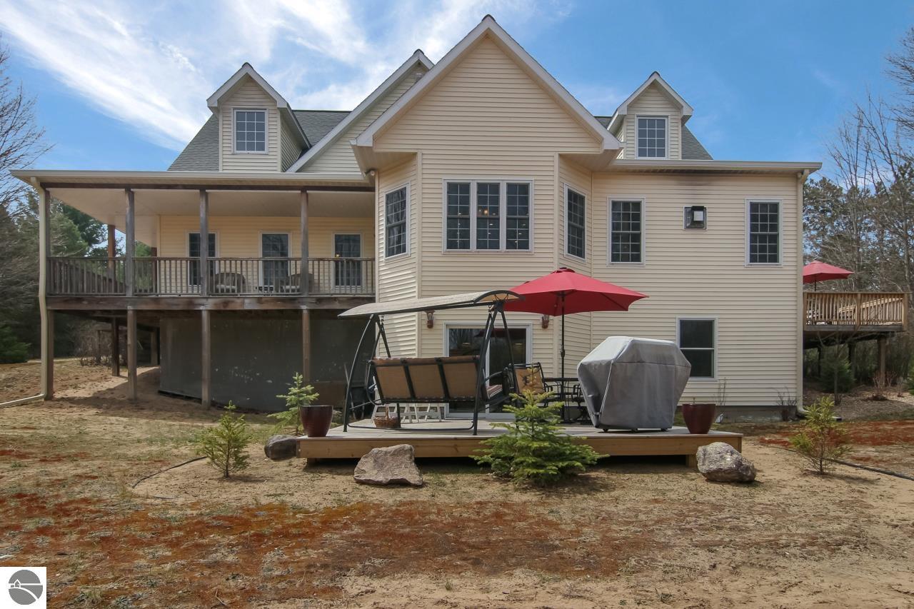 Rear of a beige two-story house with a covered deck and a raised patio with red umbrellas.