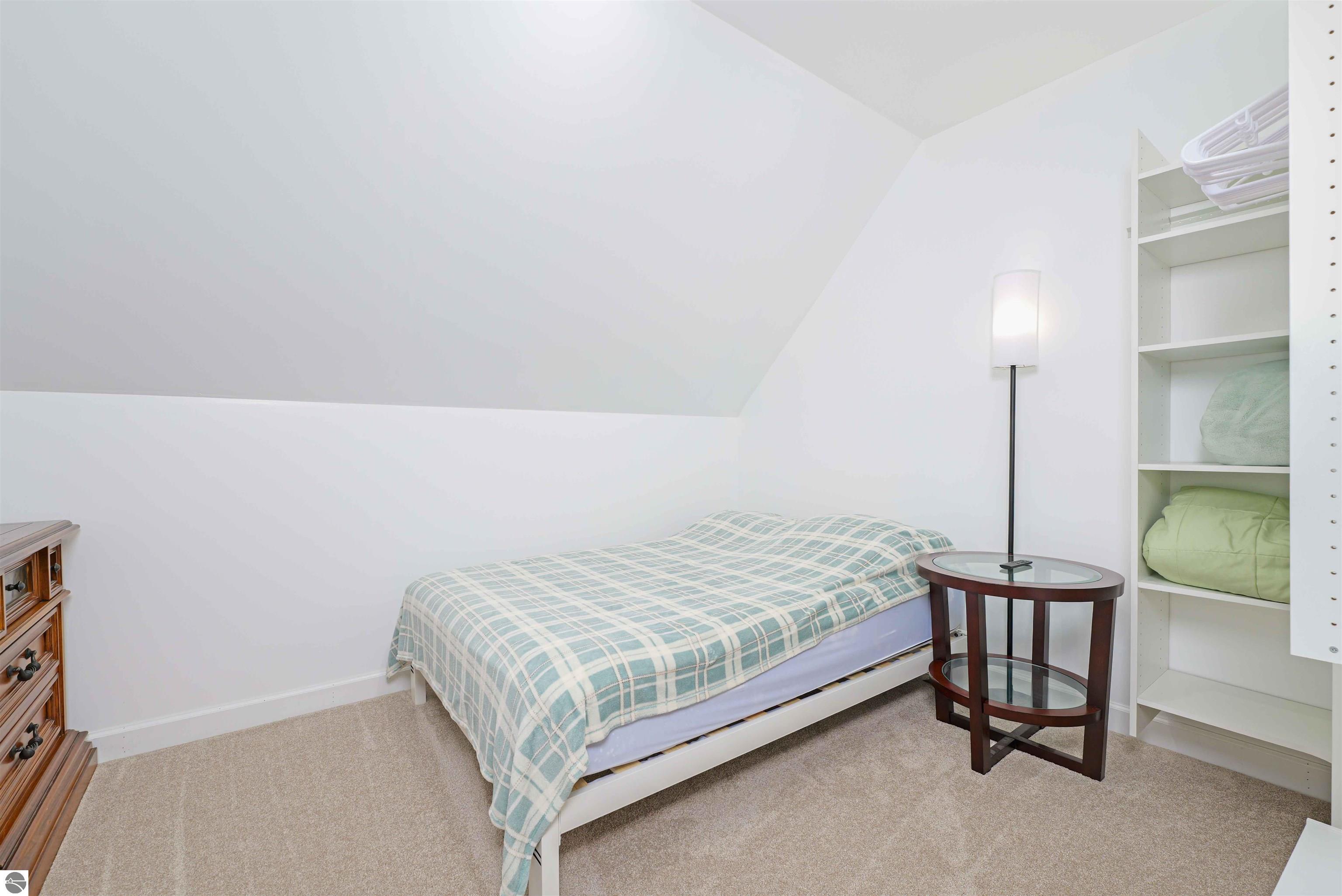 Small bedroom with a plaid-covered single bed, sloped ceiling, and built-in shelves.