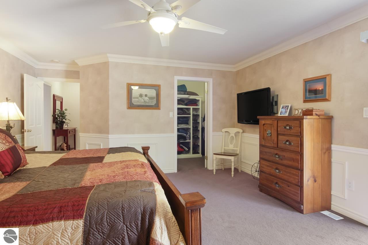 Furnished bedroom with a multicolored quilt, open clothing closet, and wooden dresser with television.