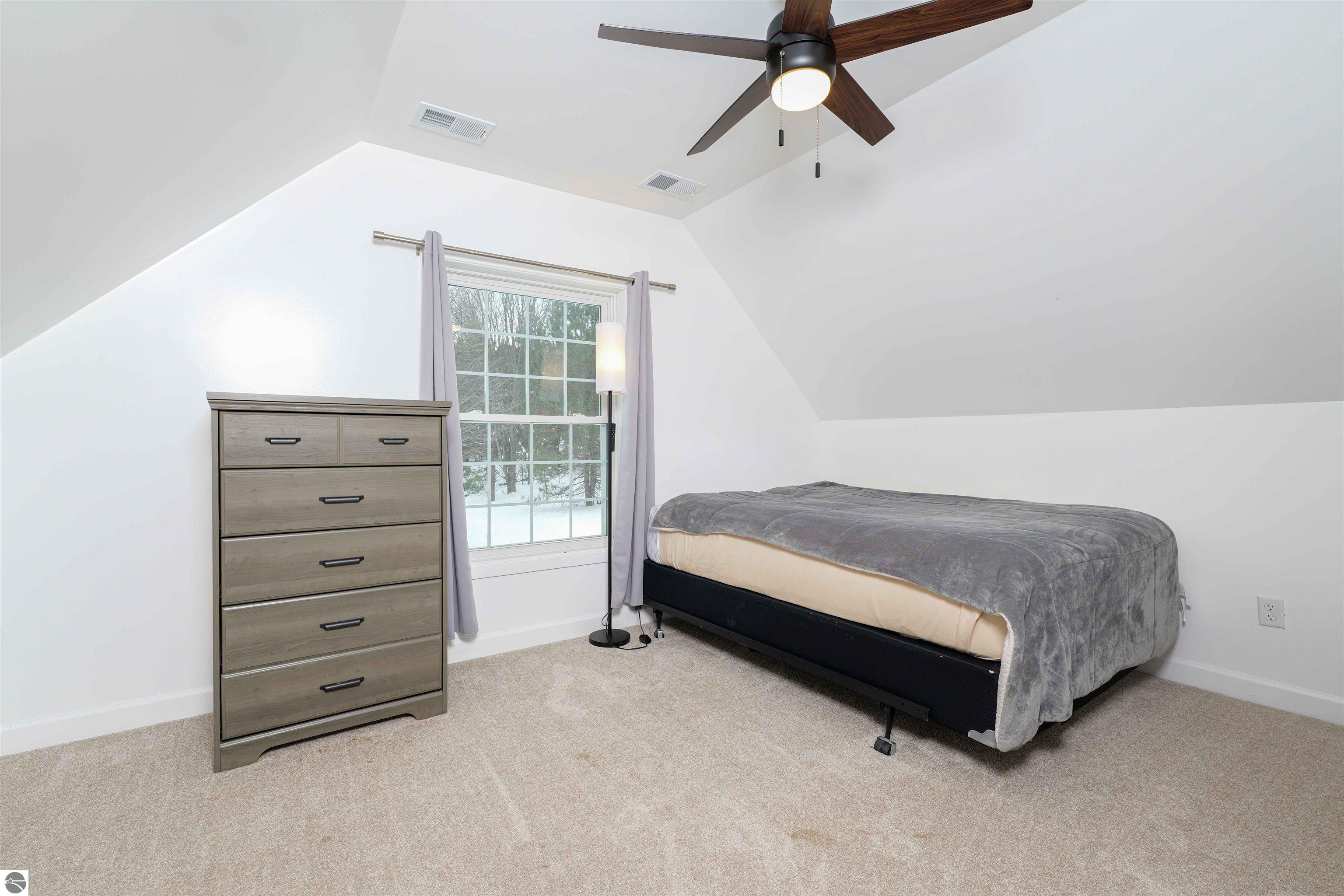 Bedroom with a gray-covered bed, wood dresser, and window overlooking snowy trees.