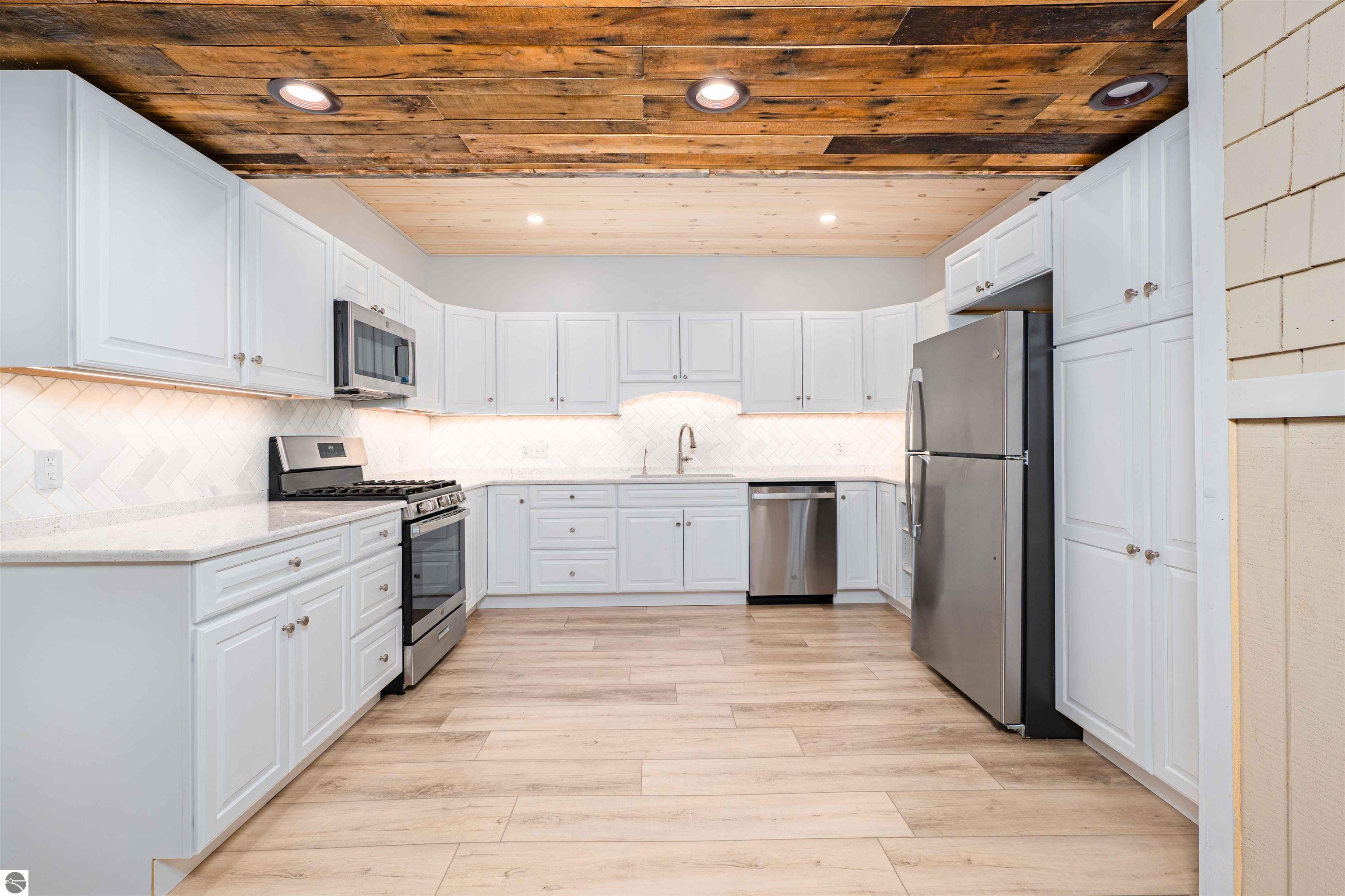 Kitchen with white cabinets, stainless steel appliances, and a rustic wood-plank ceiling.