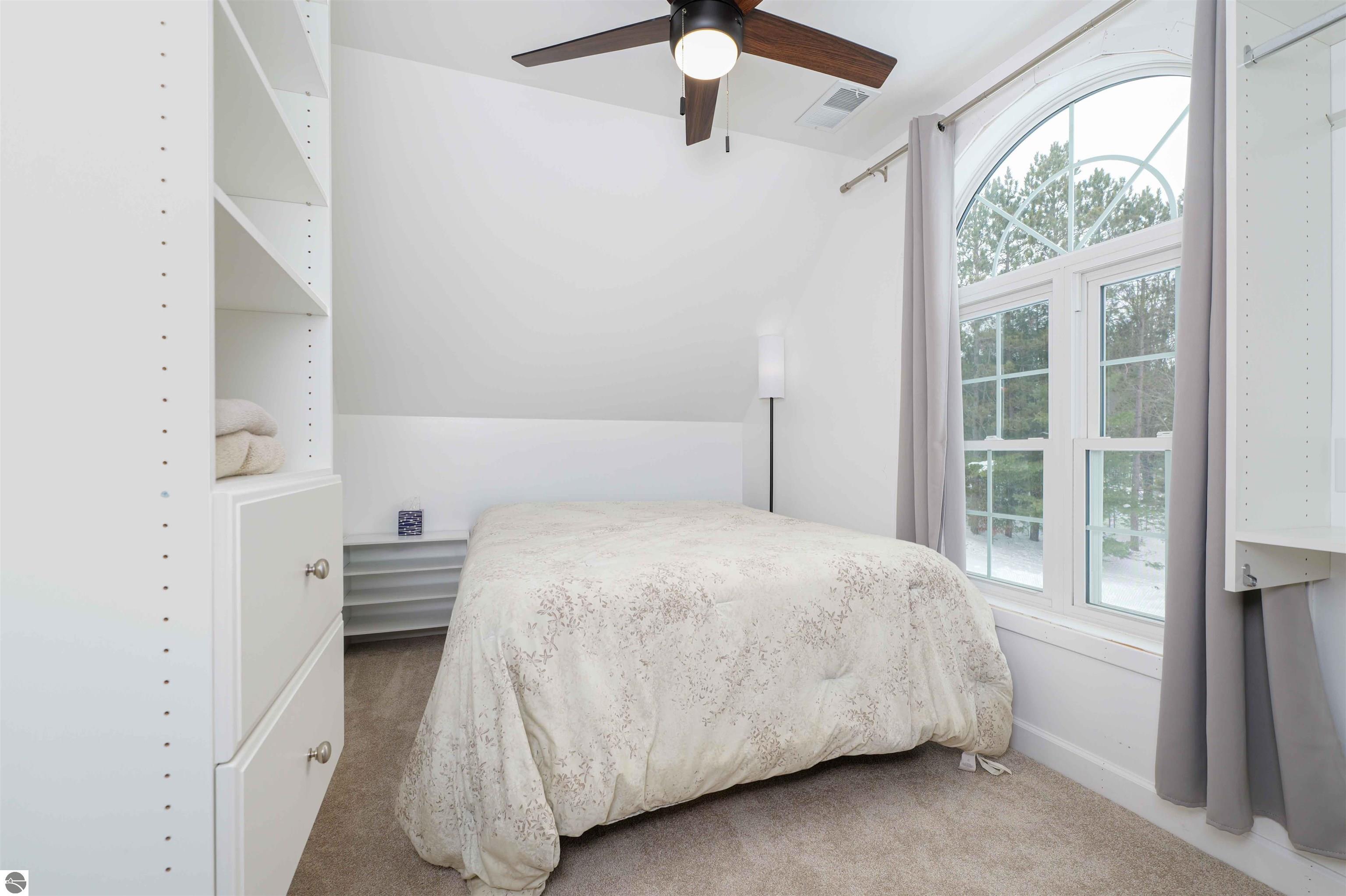 Bedroom with a floral-covered bed, built-in shelving, and a large arched window overlooking snowy trees.