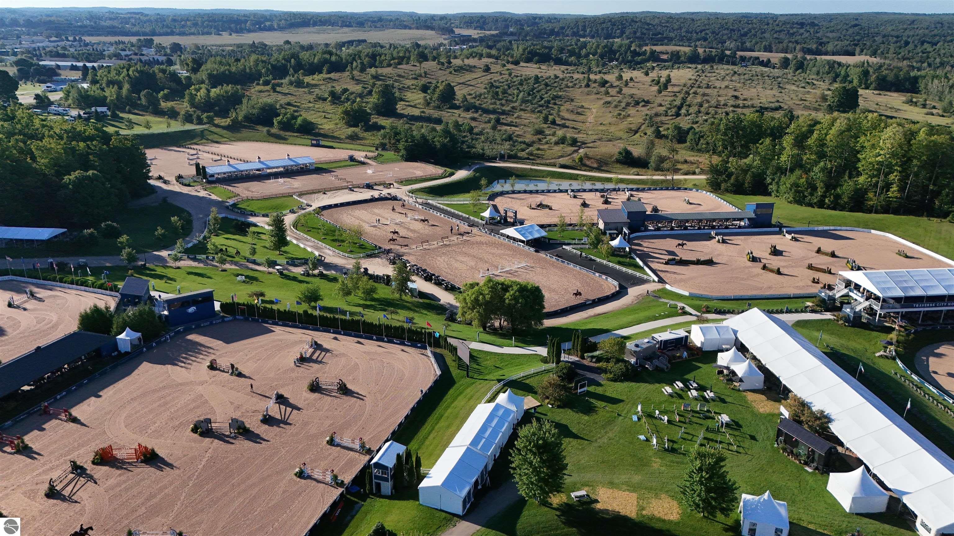 Aerial view of an equestrian venue with several riding arenas, event tents, and wooded countryside.