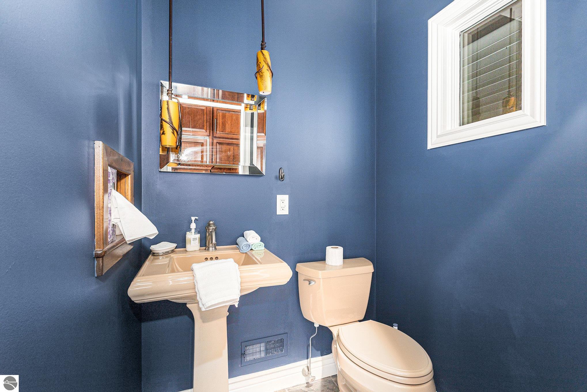 Bathroom with deep blue walls, peach pedestal sink and toilet, and a high window.