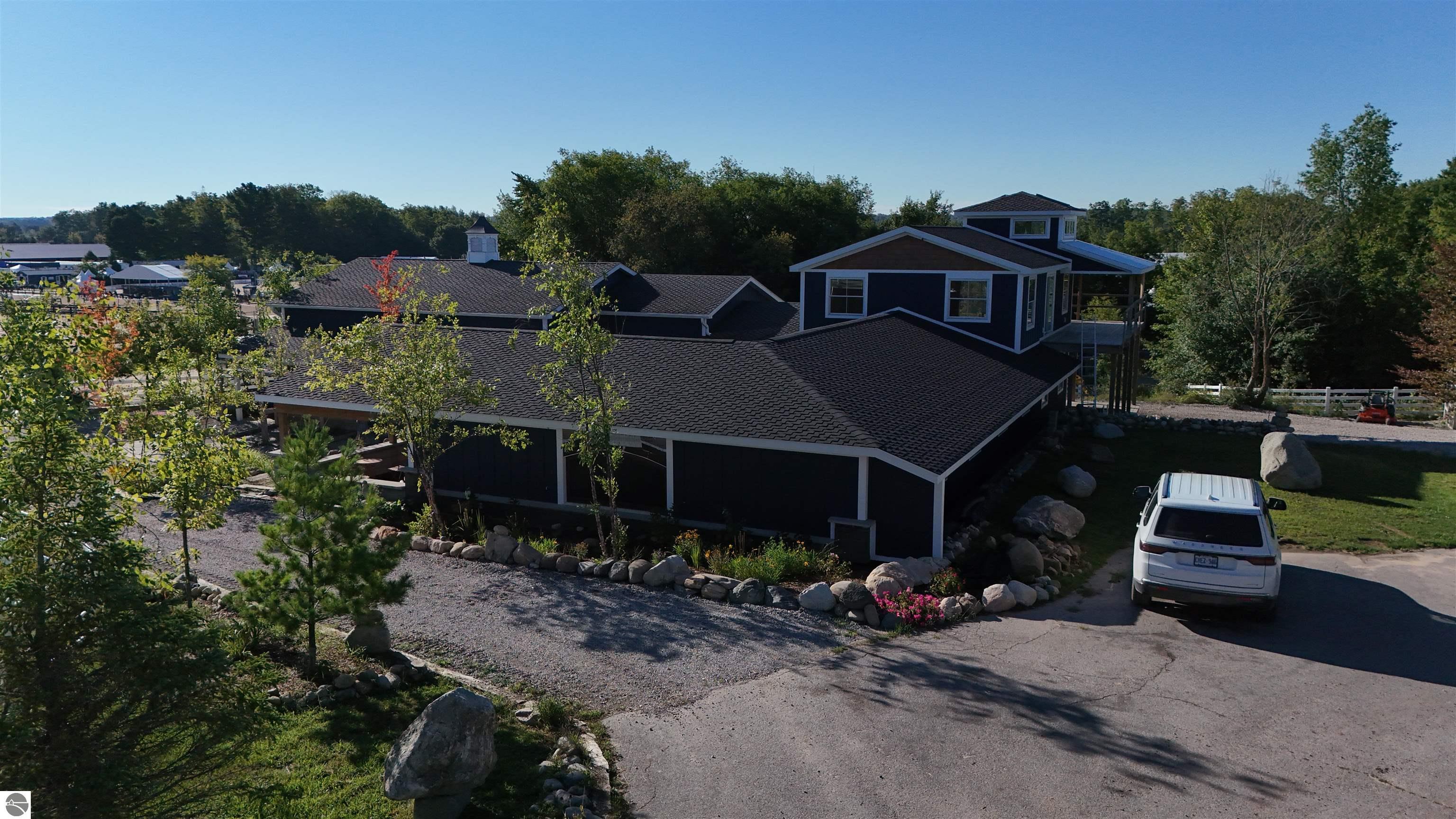 Elevated view of a dark-blue equestrian property with connected buildings, landscaped grounds, and a gravel drive.