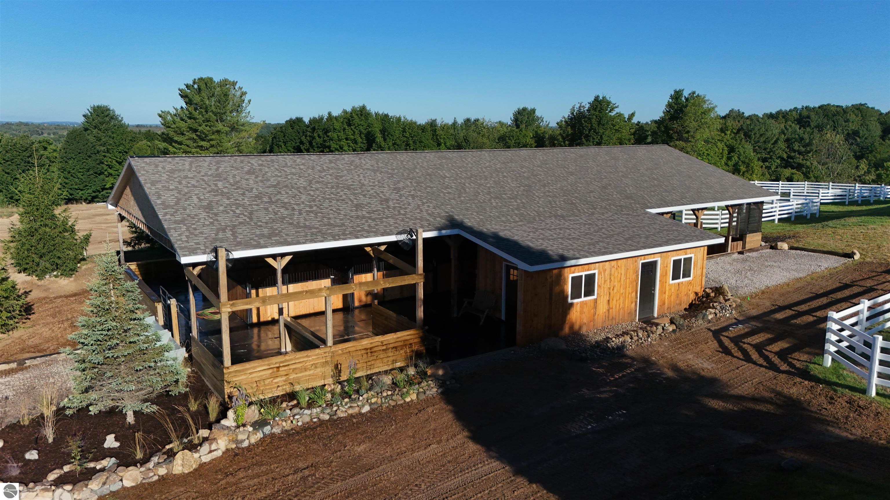 Horse barn with a covered stall area and white paddock fencing, viewed from above.