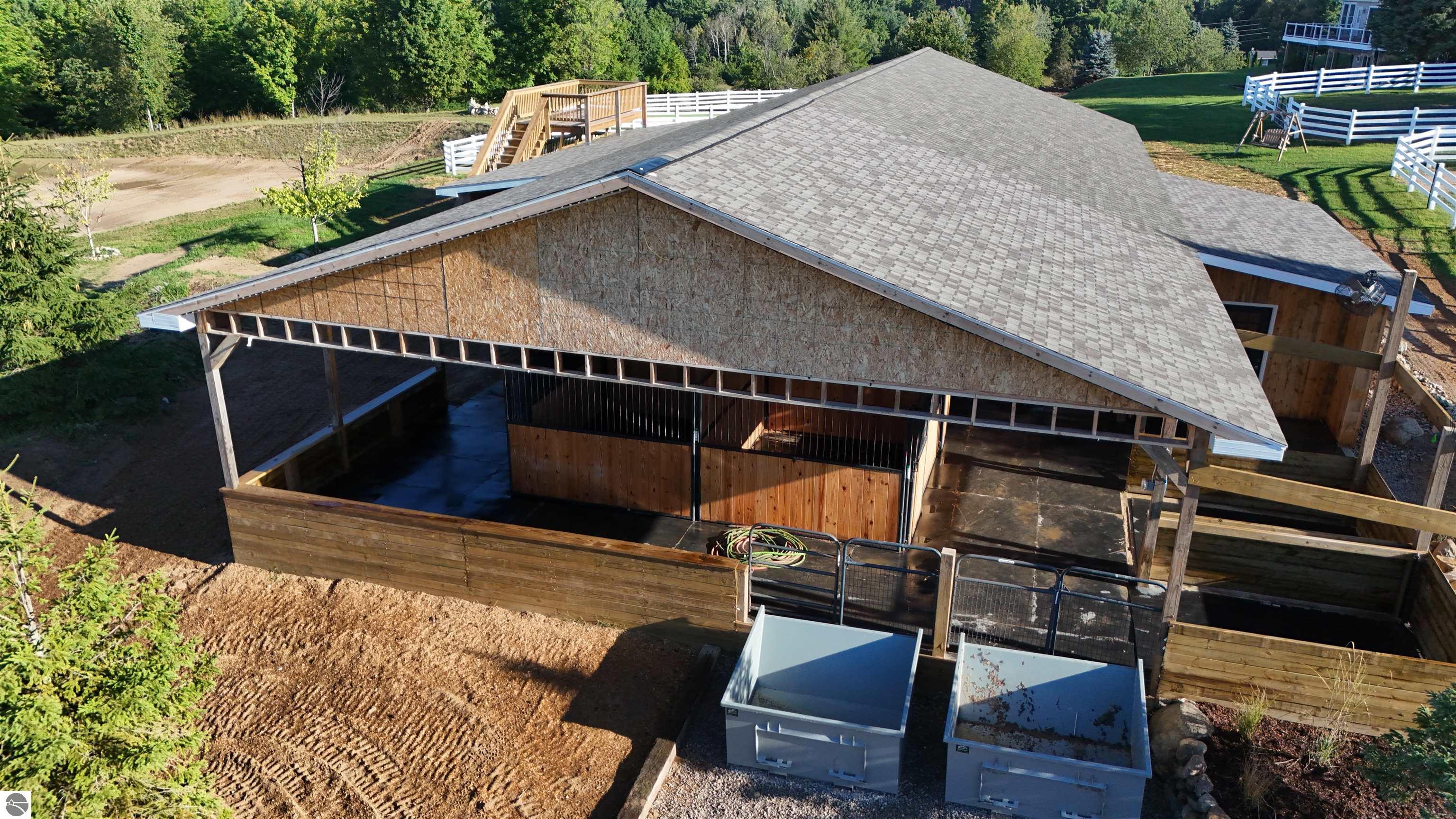 Aerial view of a wooden horse barn under construction, with open stalls and white-fenced paddocks.