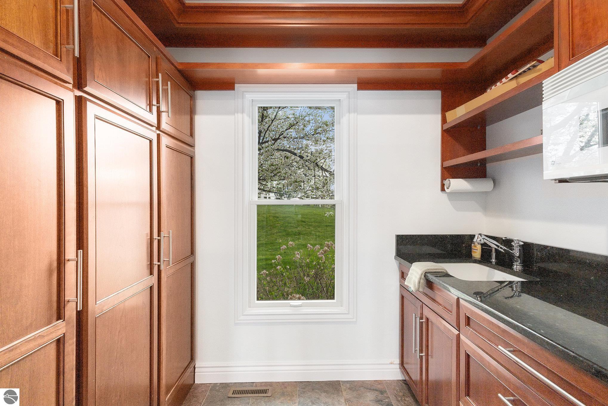 Bathroom with extensive wood cabinetry, a dark sink counter, and a window overlooking a flowering tree.