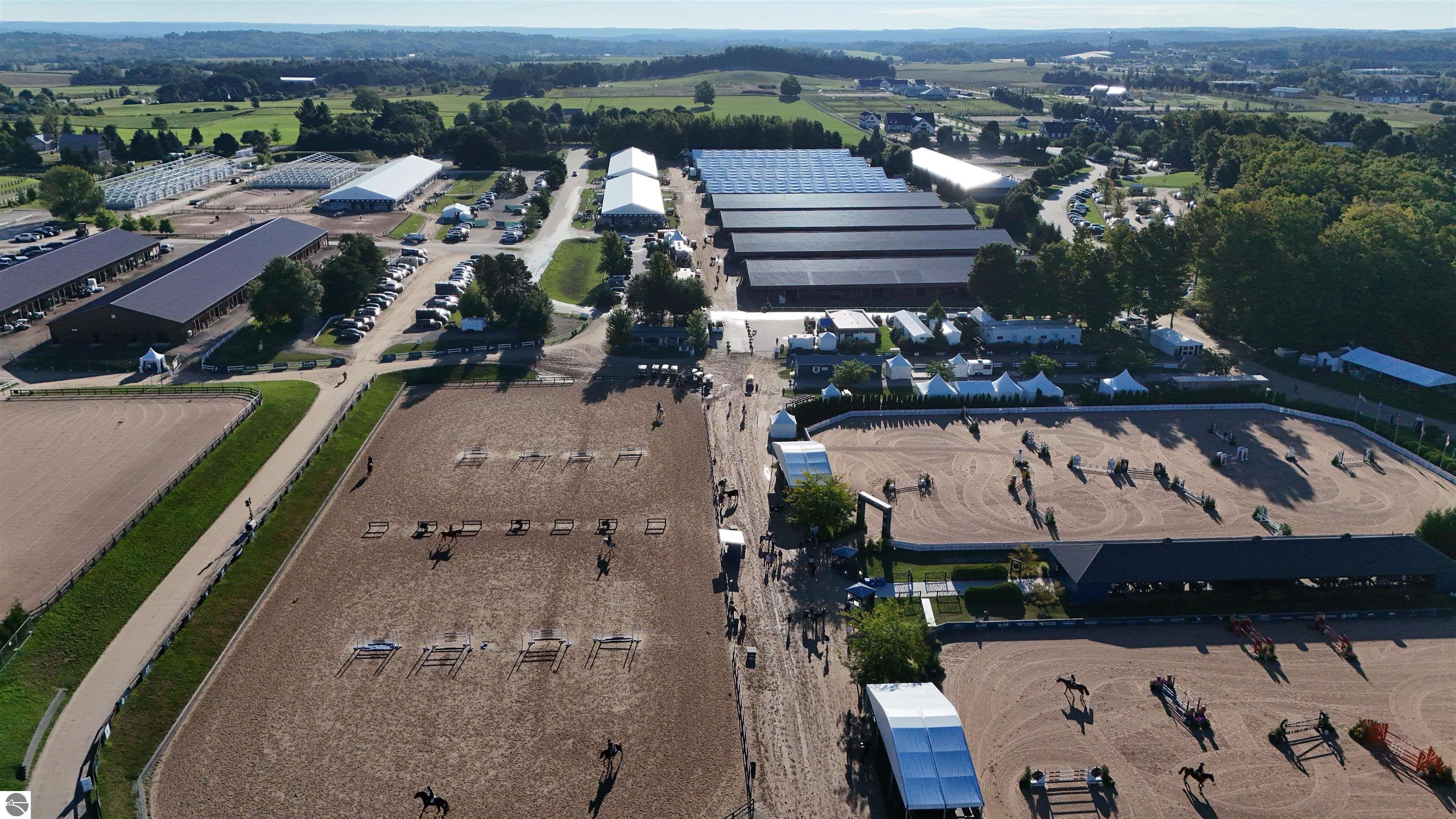Aerial view of an equestrian facility with several riding arenas, barns, and jumping courses.