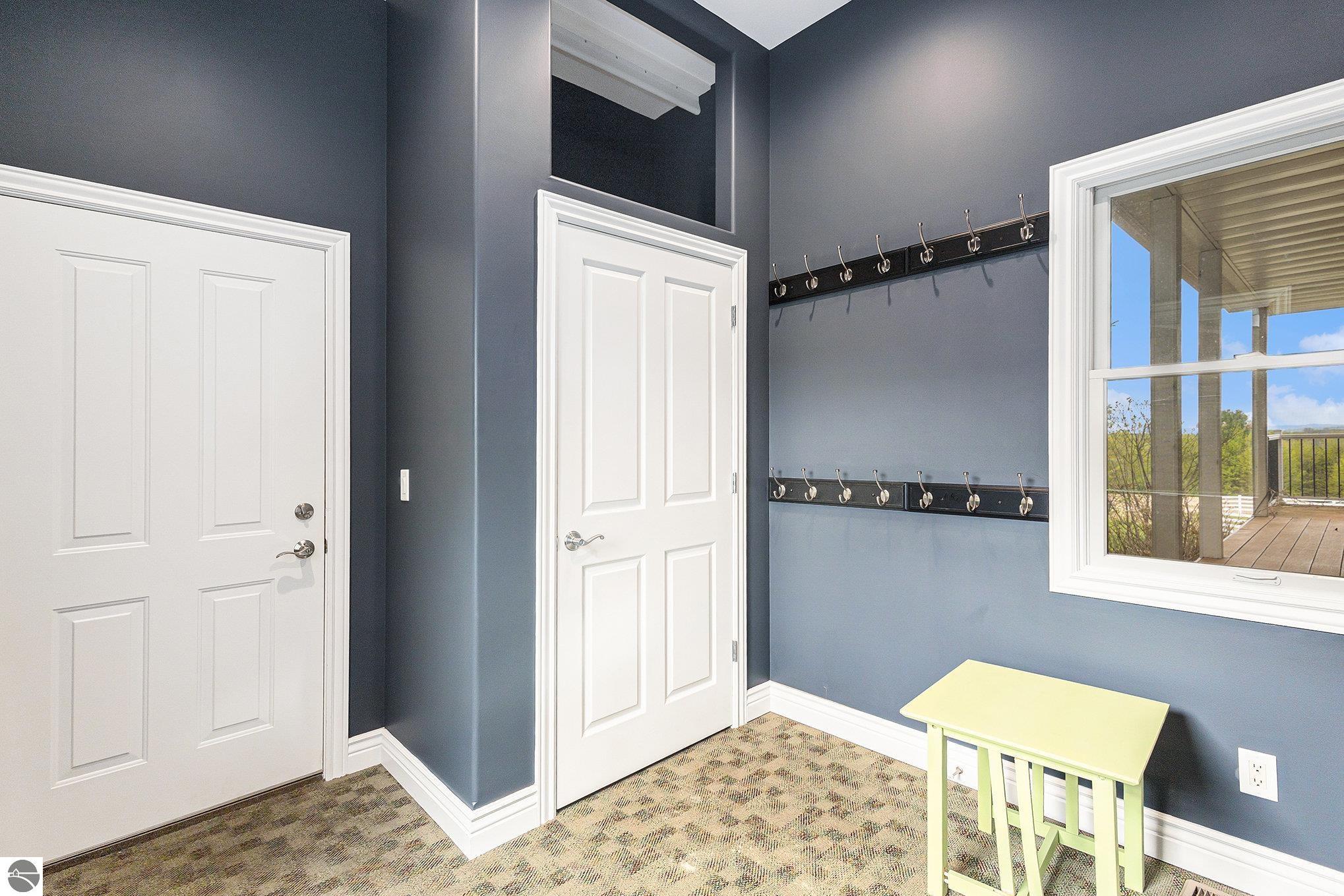 Entryway with rows of coat hooks, white paneled doors, and a window overlooking a covered deck.