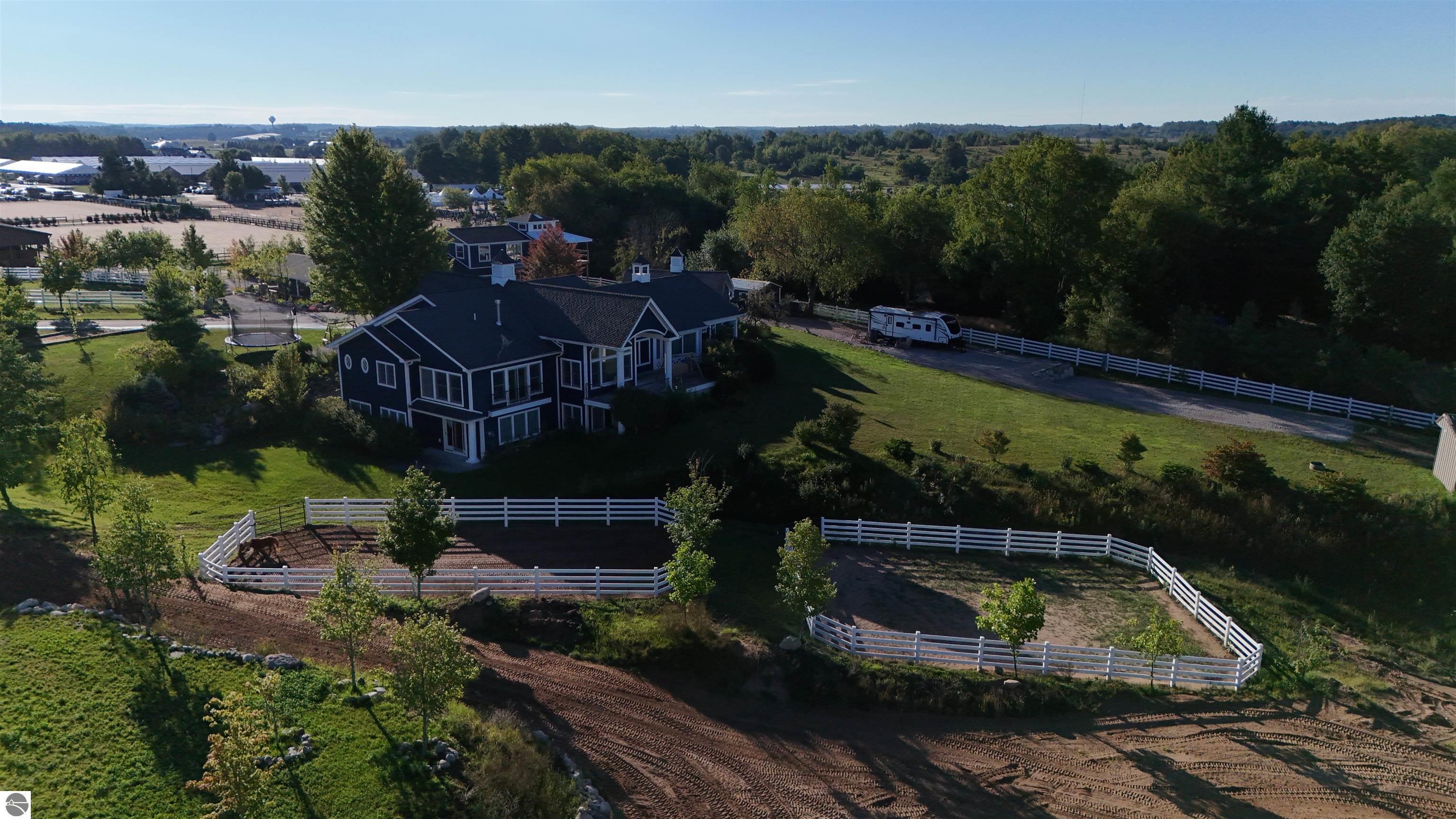 Aerial view of a home with white-fenced horse paddocks and a horse.