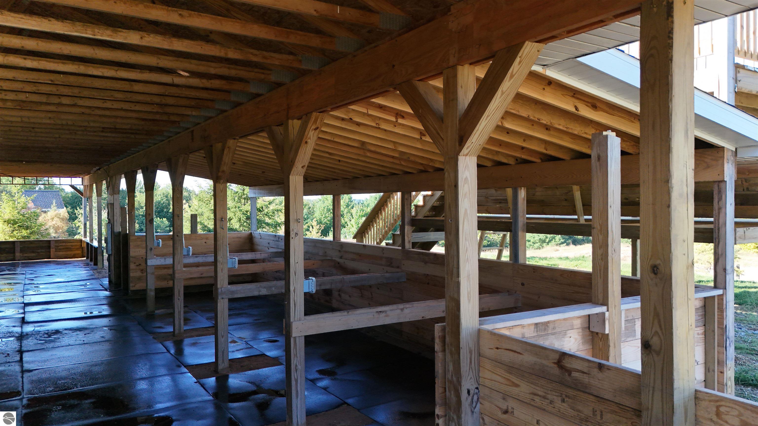 Wooden horse barn interior with stall partitions, timber framing, and rubber-mat flooring.