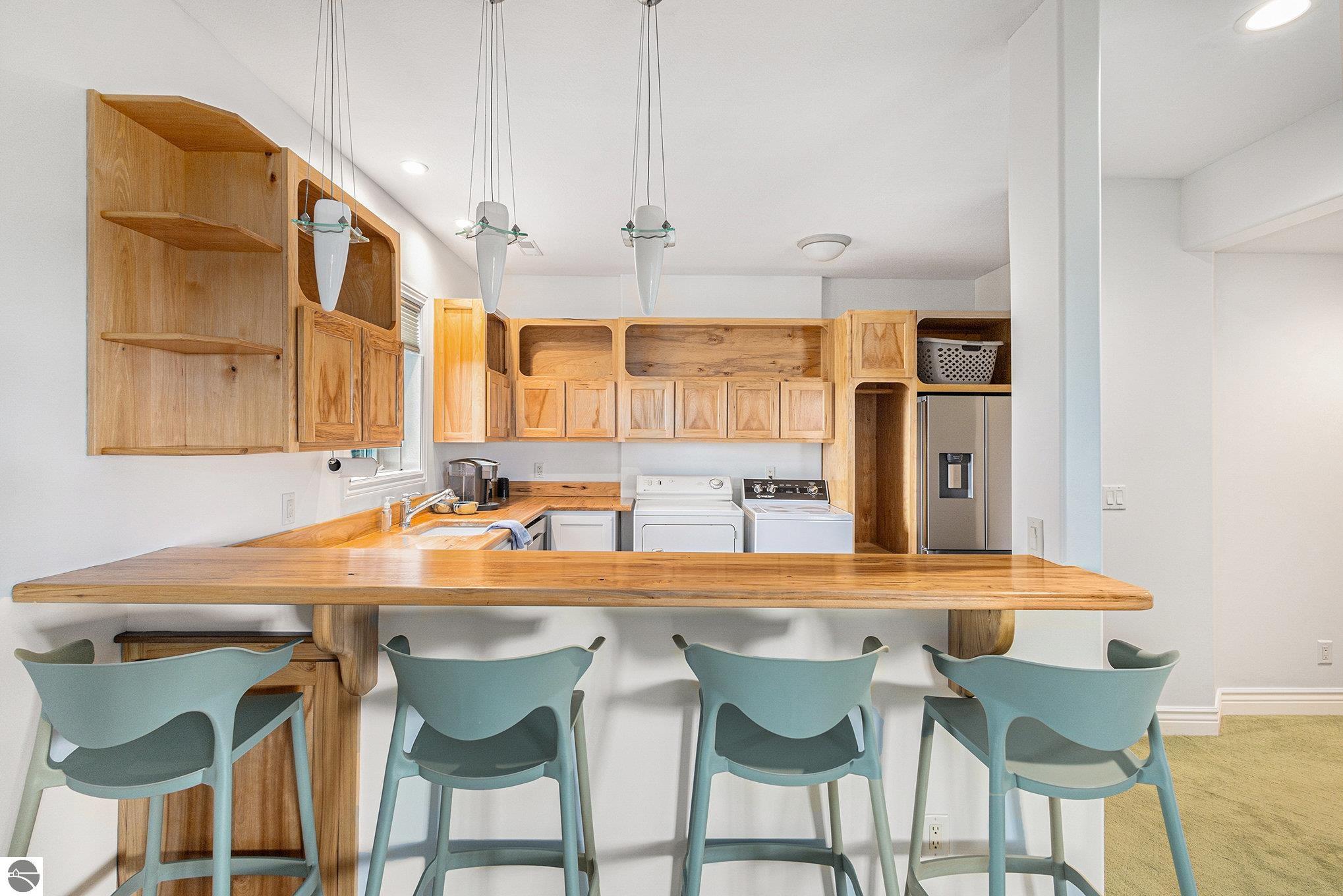 Laundry room with wood cabinetry, washer and dryer, and a breakfast bar with pale blue chairs.