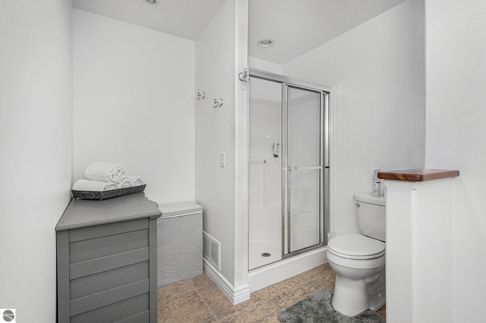 Bathroom with a glass shower, toilet, and gray cabinet topped with folded towels.