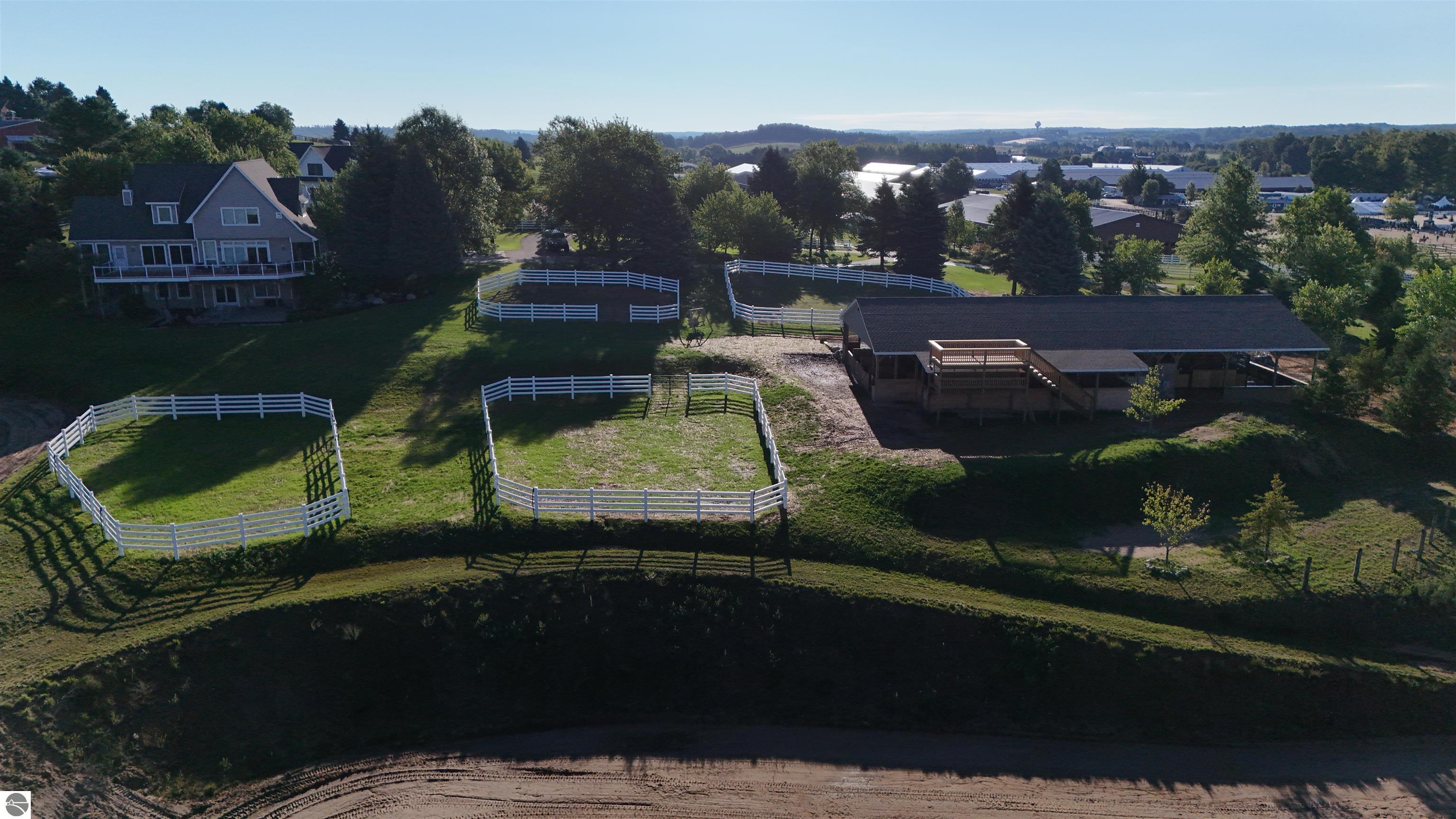 Aerial view of a house, stable, and several white-fenced paddocks.
