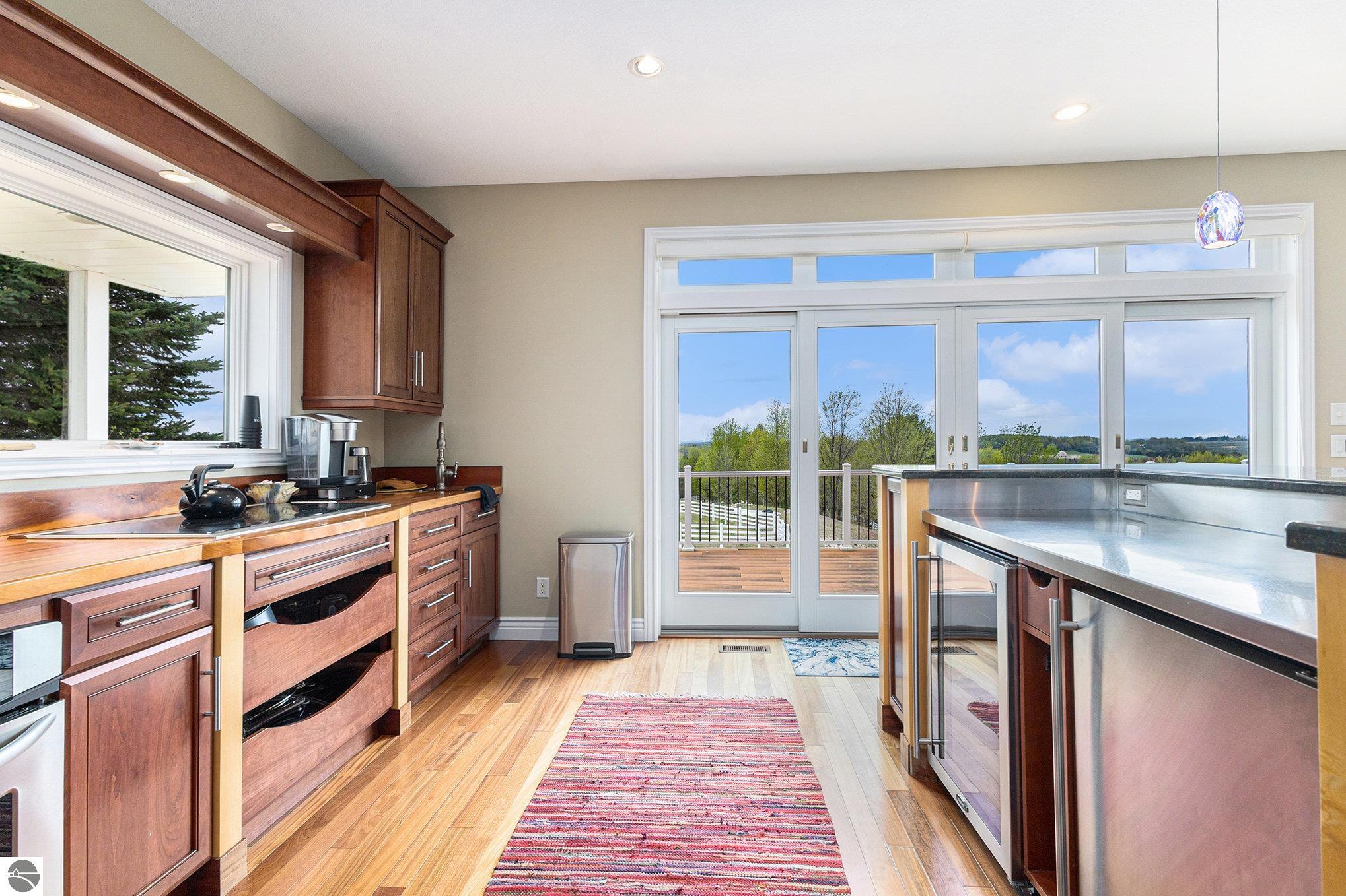 Kitchen with warm wood cabinetry, a large metal-topped island, and glass doors overlooking a deck and water.