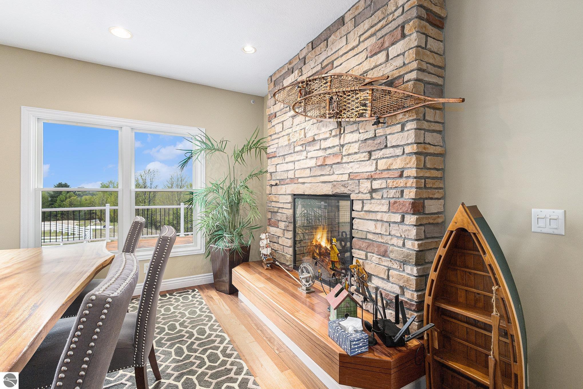 Dining area with a stone fireplace, canoe decor, and large windows overlooking a fenced lawn.