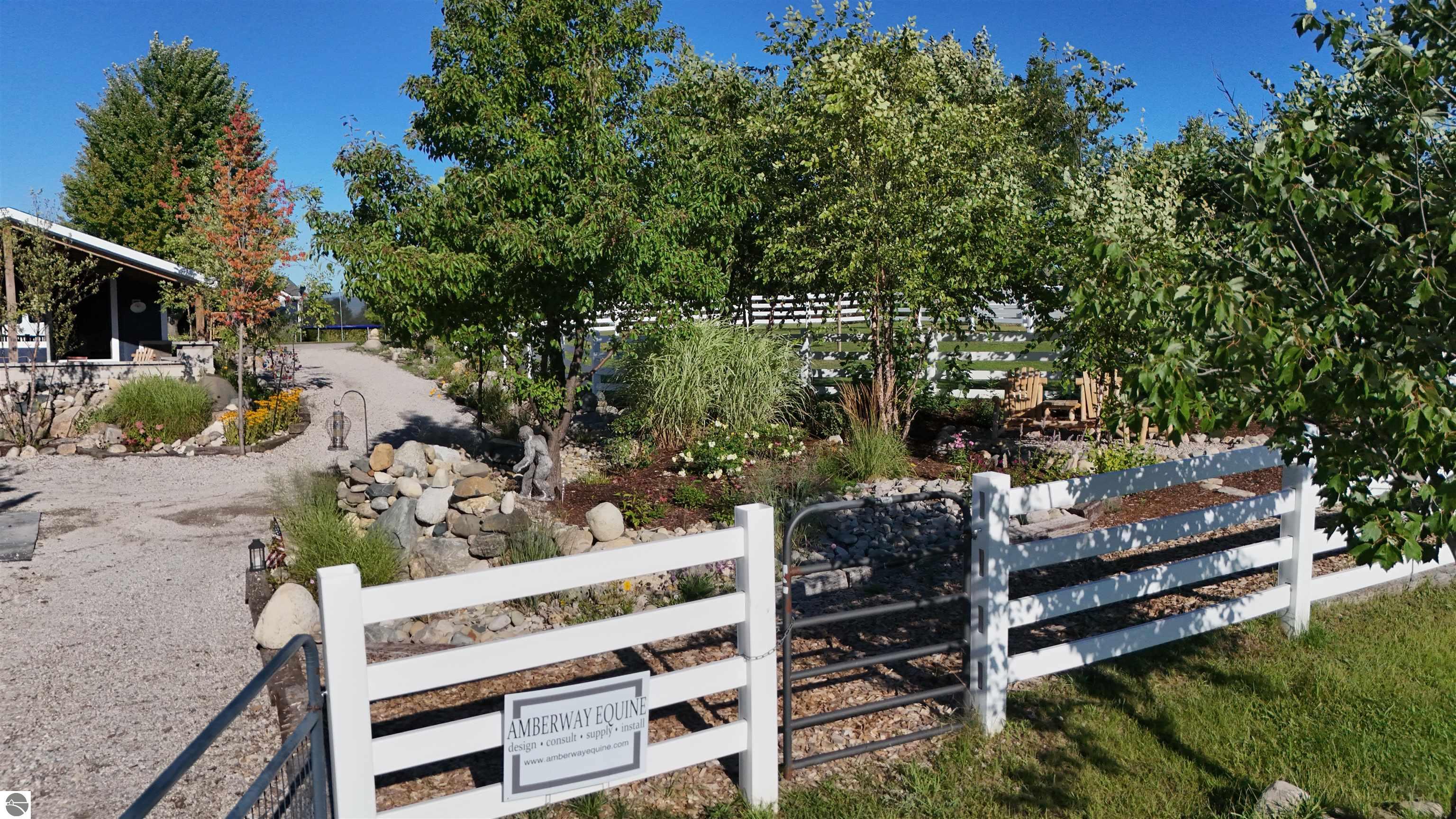 Equestrian property entrance with a white fence, metal gate, landscaped garden, and Amberway Equine sign.
