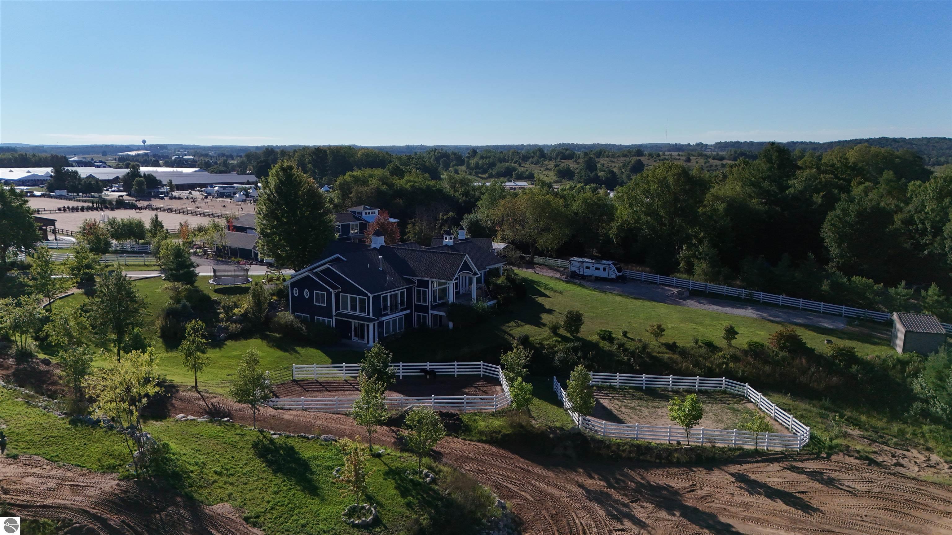 Aerial view of a dark two-story home with white-fenced paddocks and wooded grounds.